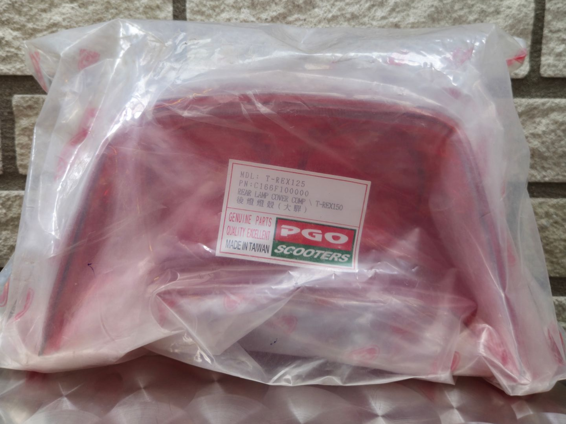 Een in plastic verpakte rode tas met een wit etiket op een stenen ondergrond.