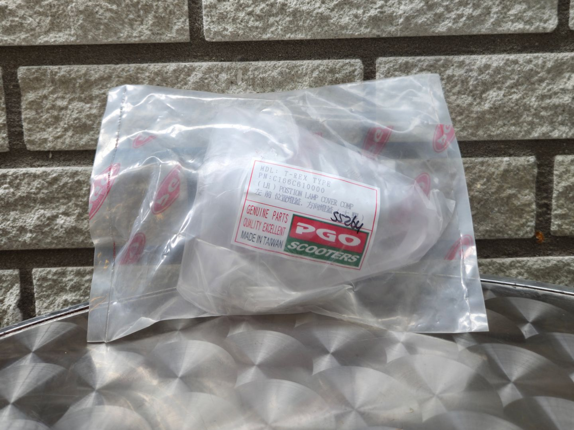 Een doorzichtige plastic zak met een klein rood-wit etiket op een metalen oppervlak tegen een bakstenen muur.