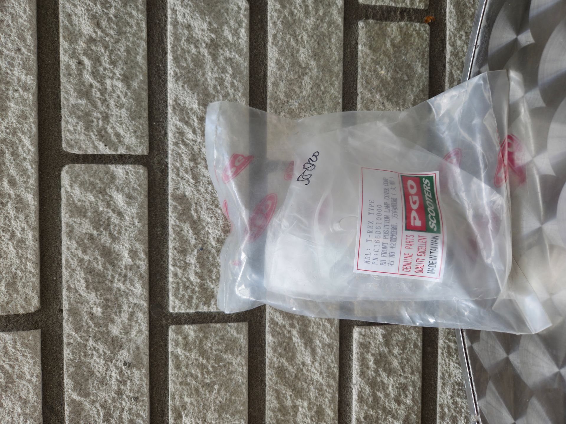 Een doorzichtige plastic zak met een rood-wit etiket ligt op een vloer van bakstenen met een structuur.