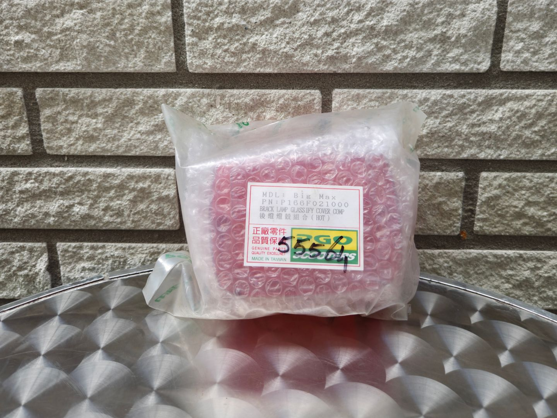 Een doorzichtige plastic zak met roze verpakte goederen en een etiket, die op een metalen tafel tegen een bakstenen muur staat.