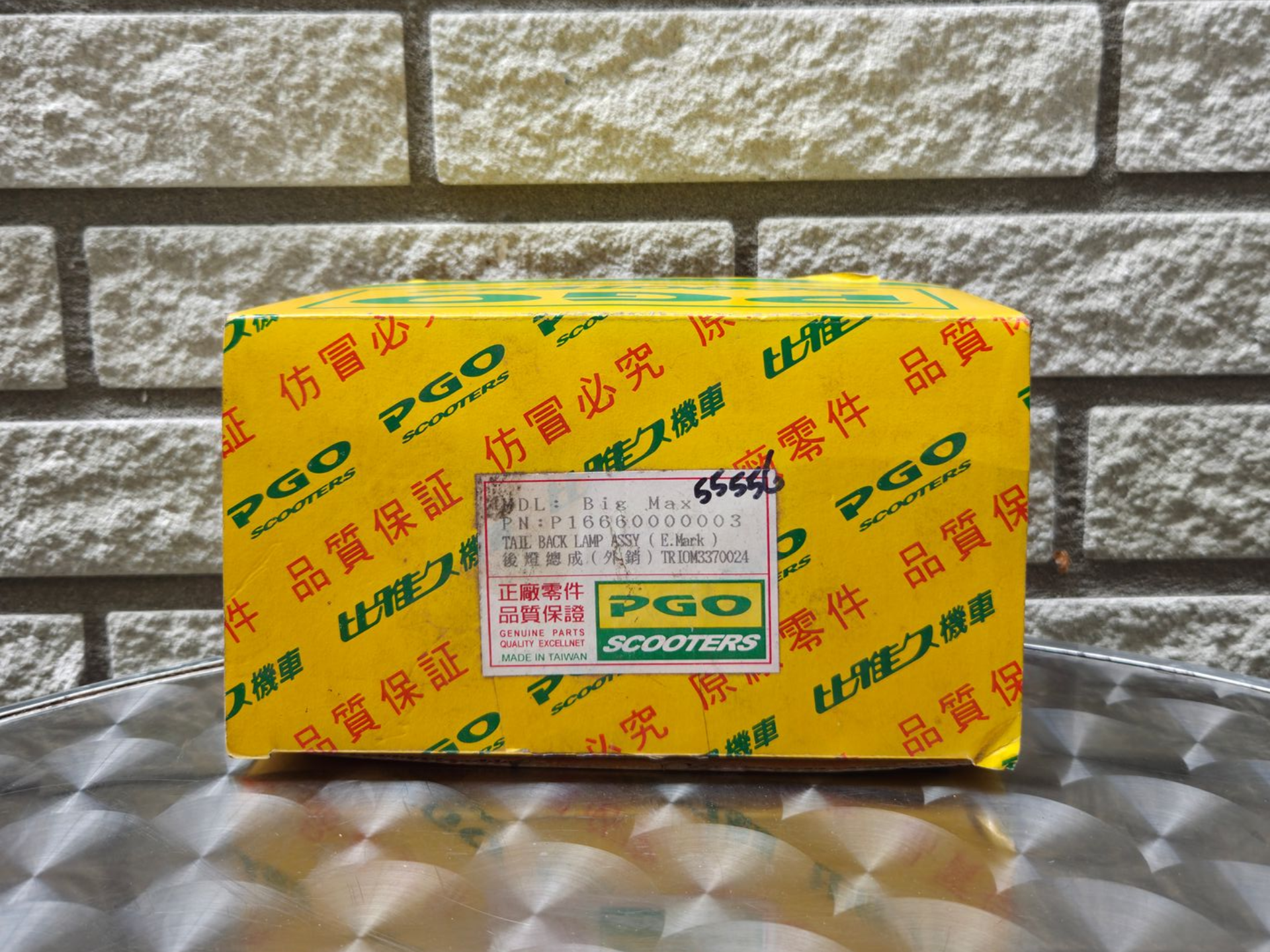 Gele productdoos met rode en groene Chinese tekst op een reflecterende tafel tegen een bakstenen muur.