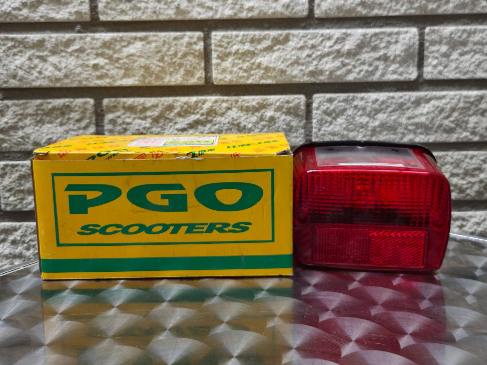 Gele productdoos met rode en groene Chinese tekst op een reflecterende tafel tegen een bakstenen muur.
