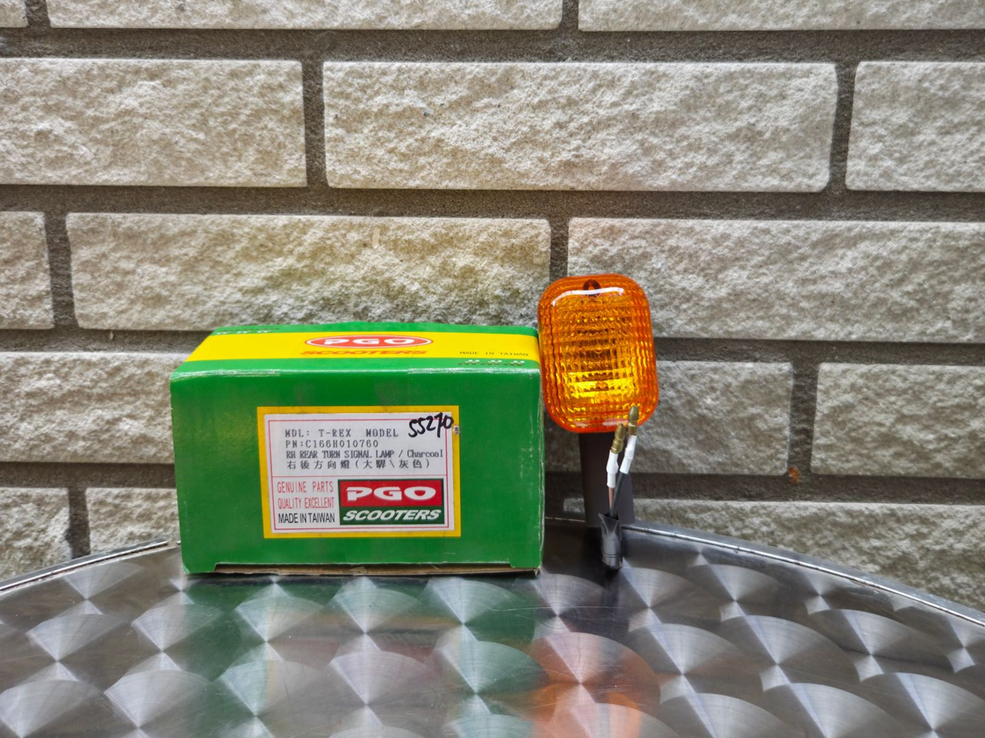 Groen-gele doos naast een amberkleurig motorfietsrichtingaanwijzerlicht op een geruite metalen ondergrond.