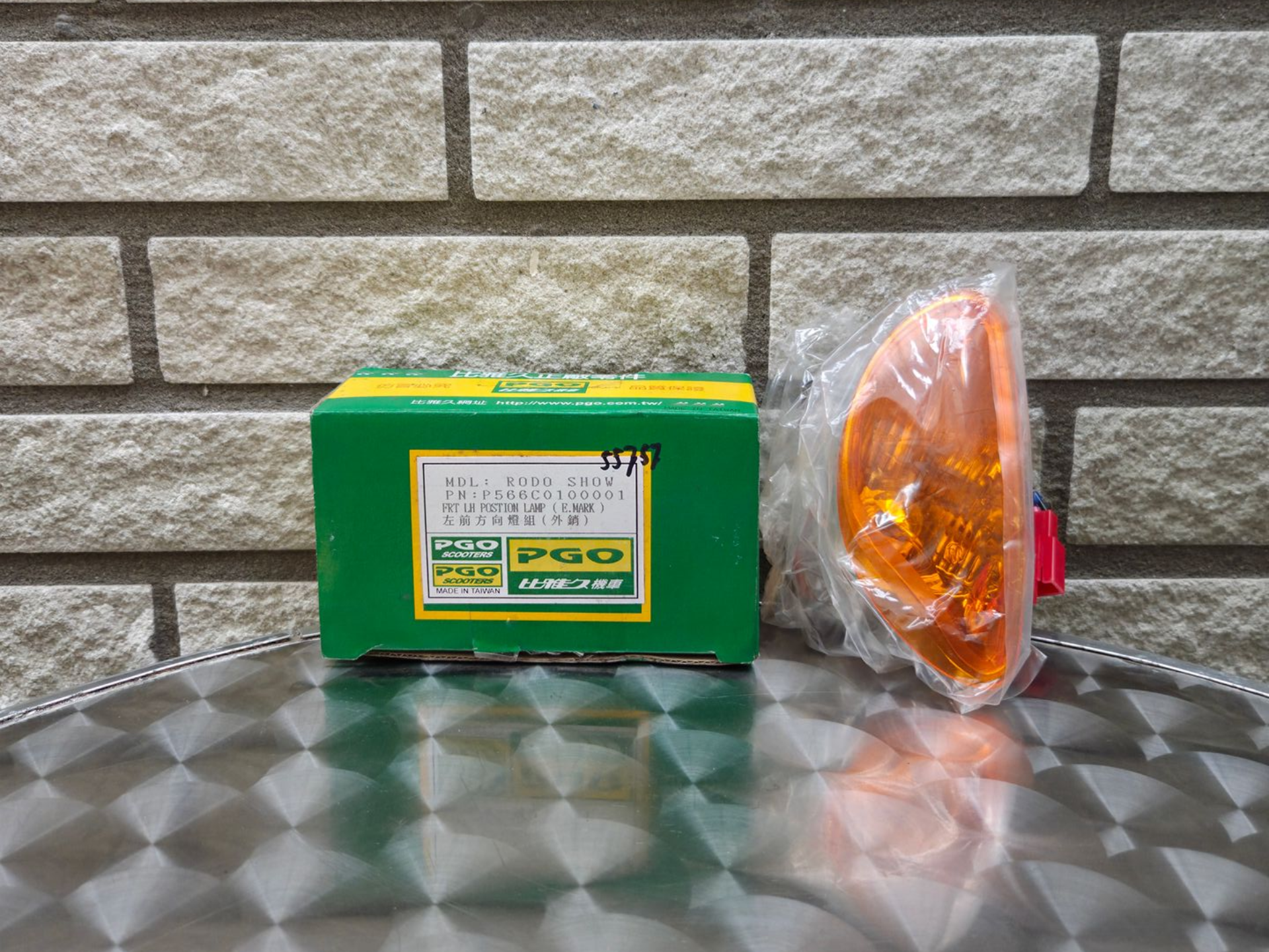 Groene doos en oranje achterlichtlens op een reflecterend oppervlak tegen een bakstenen muur.
