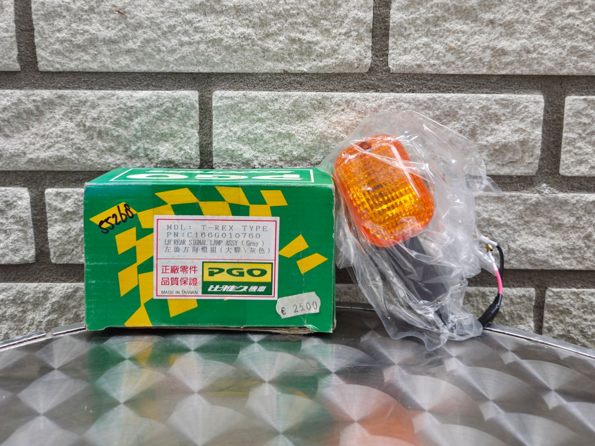 Groene doos en ingepakte oranje lamp op een metalen ondergrond tegen een grijze bakstenen muur.