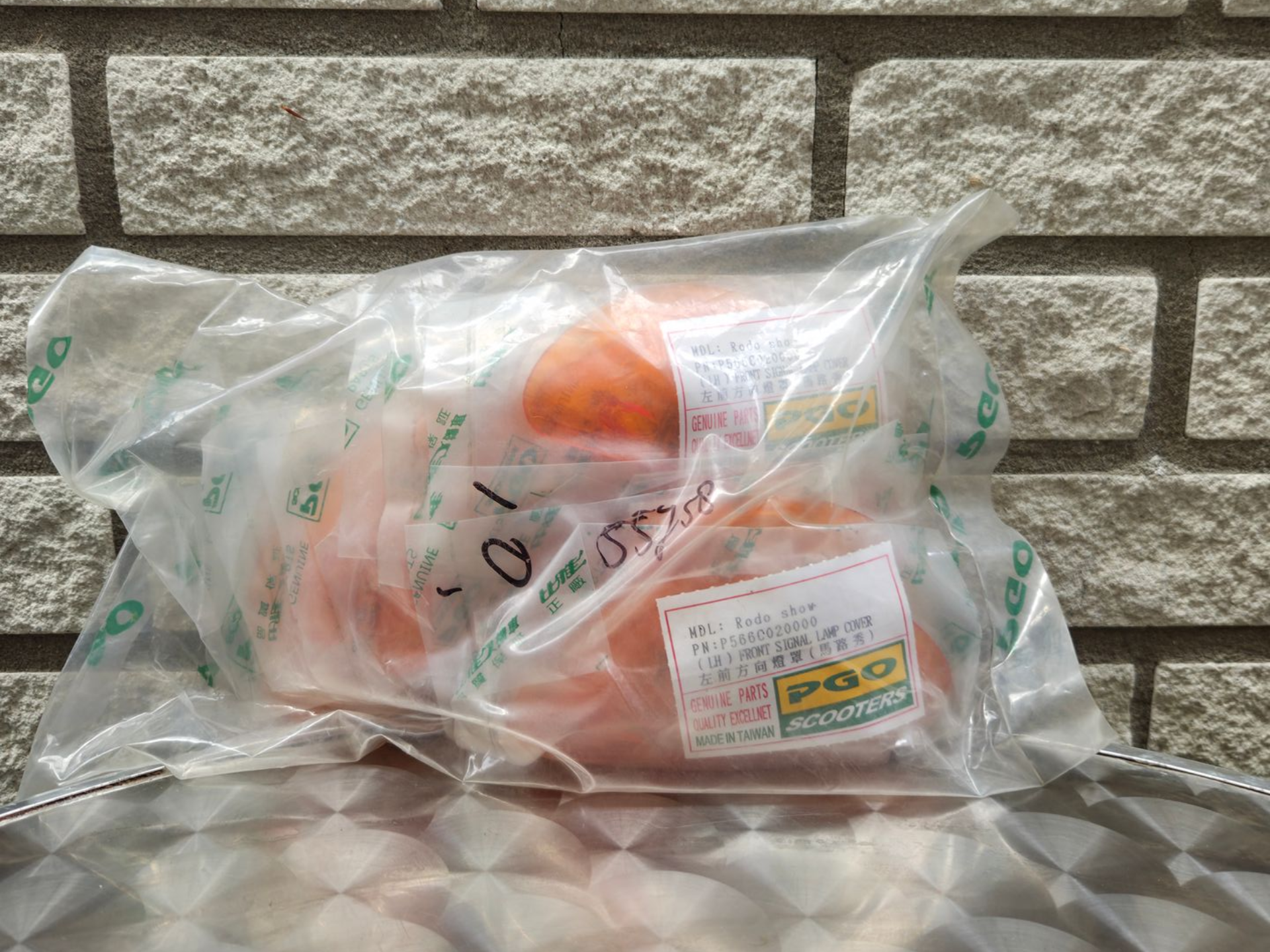 Een doorzichtige plastic zak met sinaasappels ligt op een tafel voor een bakstenen muur.