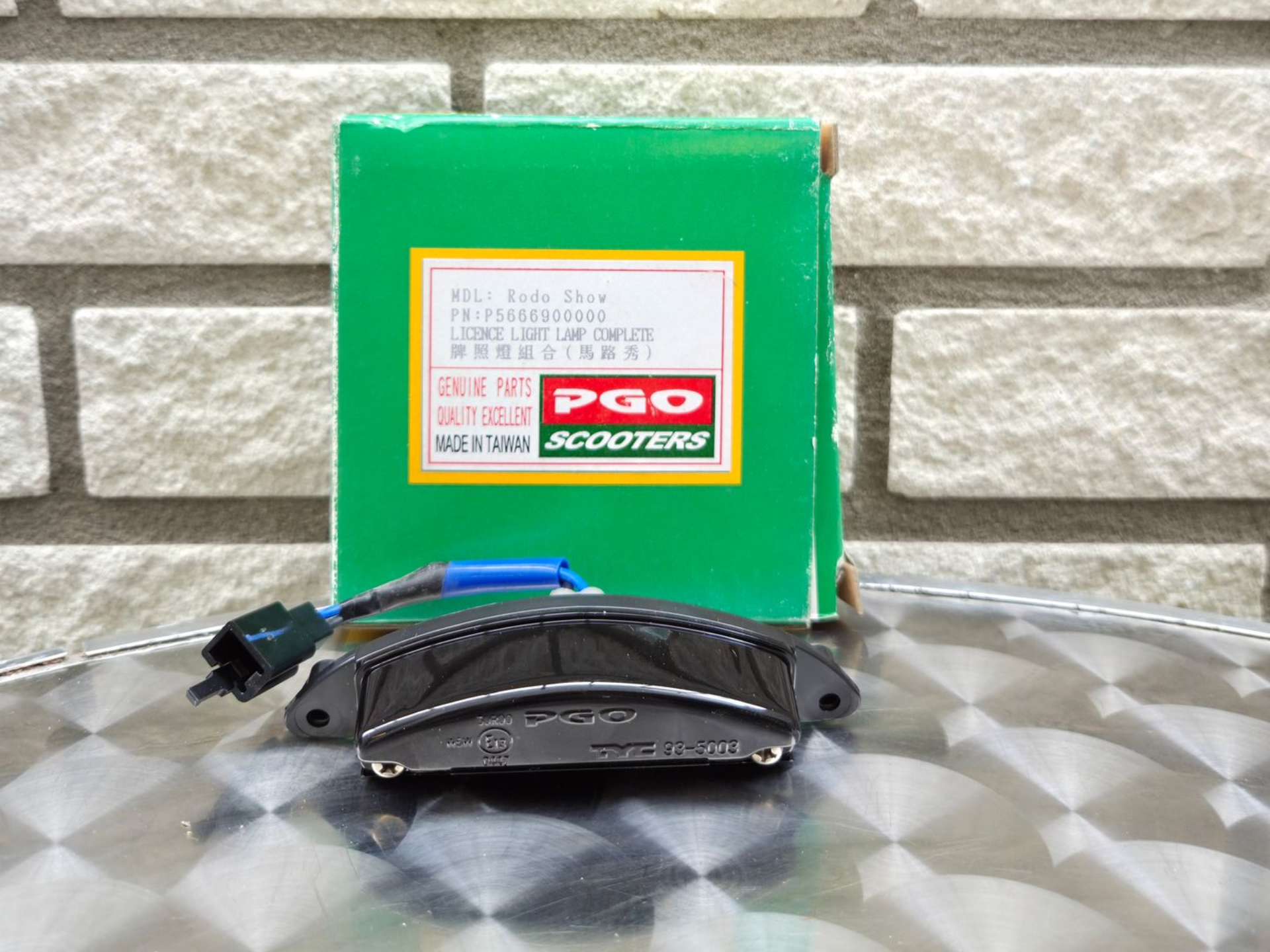 Zwarte remklauw voor een groene PGO-doos op een zilverkleurige, gewatteerde ondergrond.