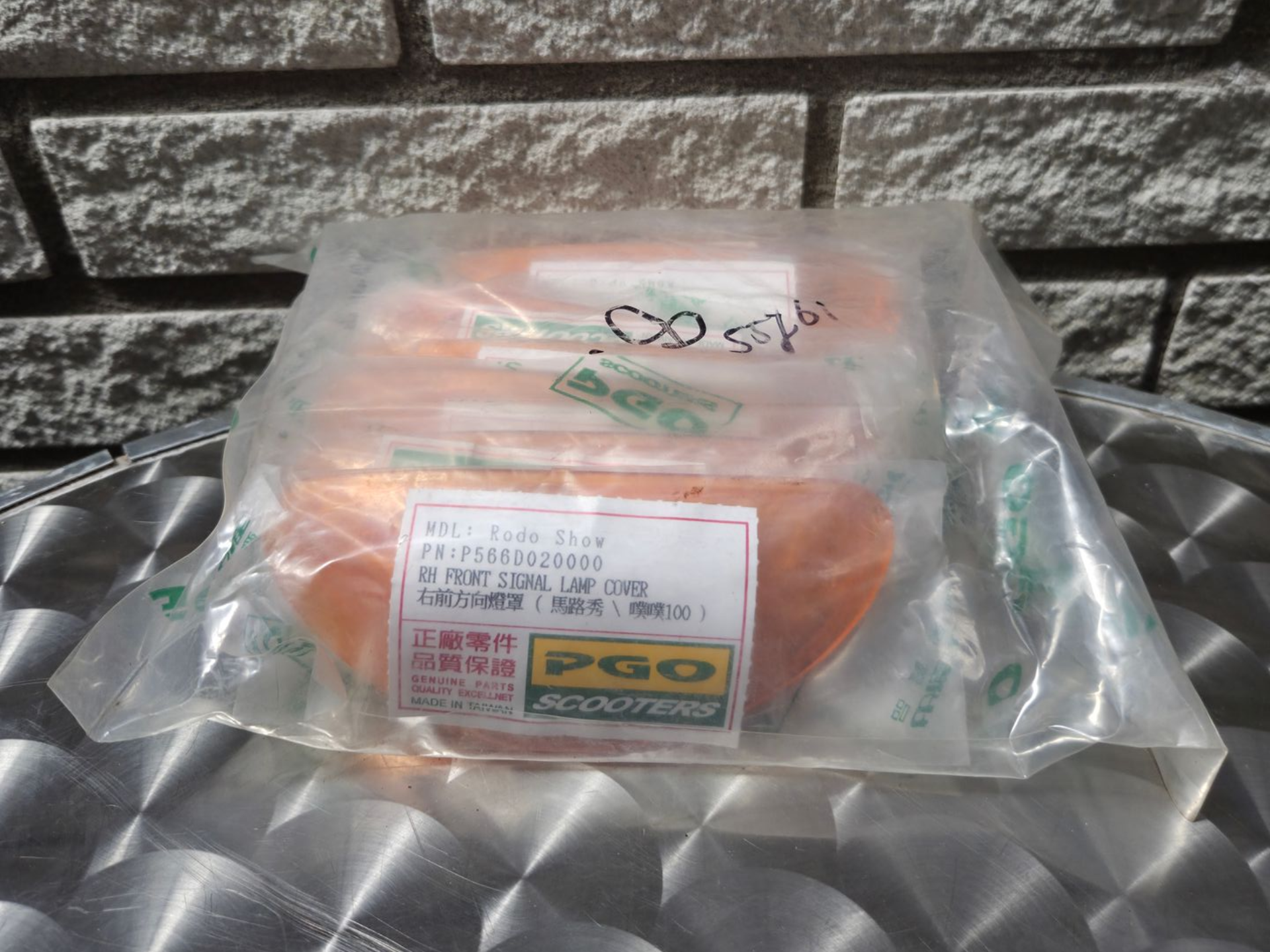 Een doorzichtige plastic zak met oranje en groene verpakte artikelen op een reflecterend metalen oppervlak tegen een bakstenen muur.