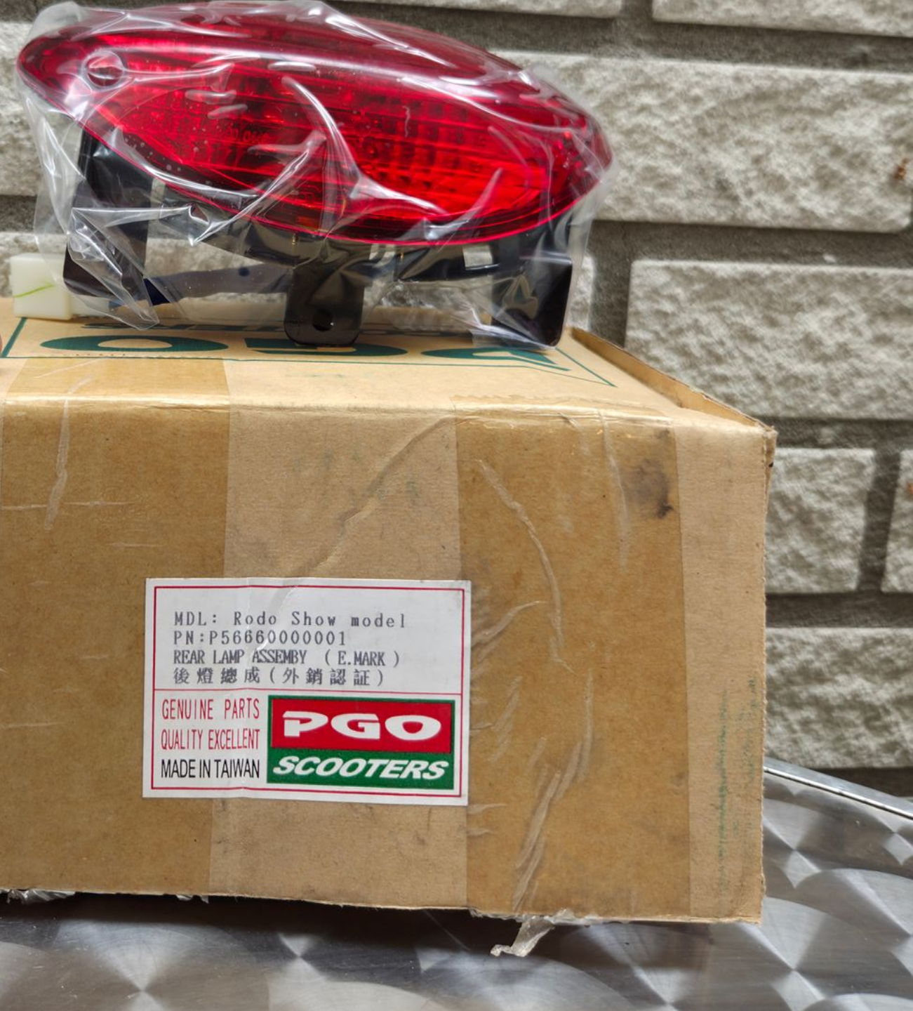 Rood scooterachterlicht op een kartonnen doos met het opschrift PGO Scooters binnen