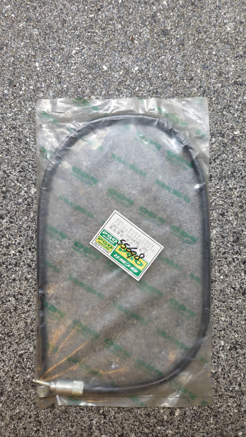 Een opgerolde zwarte slang in een doorzichtige plastic verpakking op een grijs tapijt, met een klein etiketje eraan.