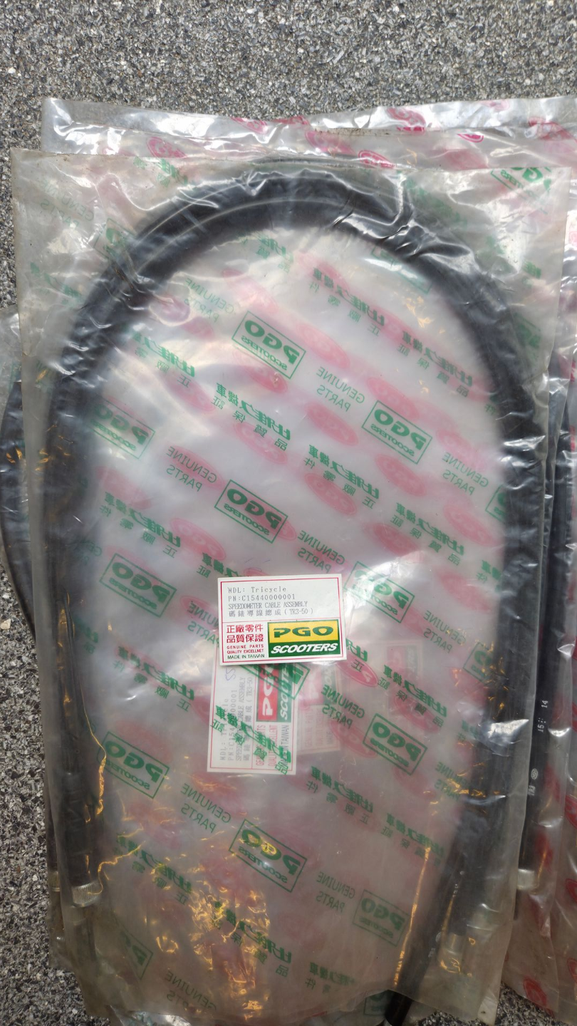 Een opgerolde zwarte kabel, verpakt in een doorzichtige plastic zak met een klein etiket op een gestructureerd grijs oppervlak.