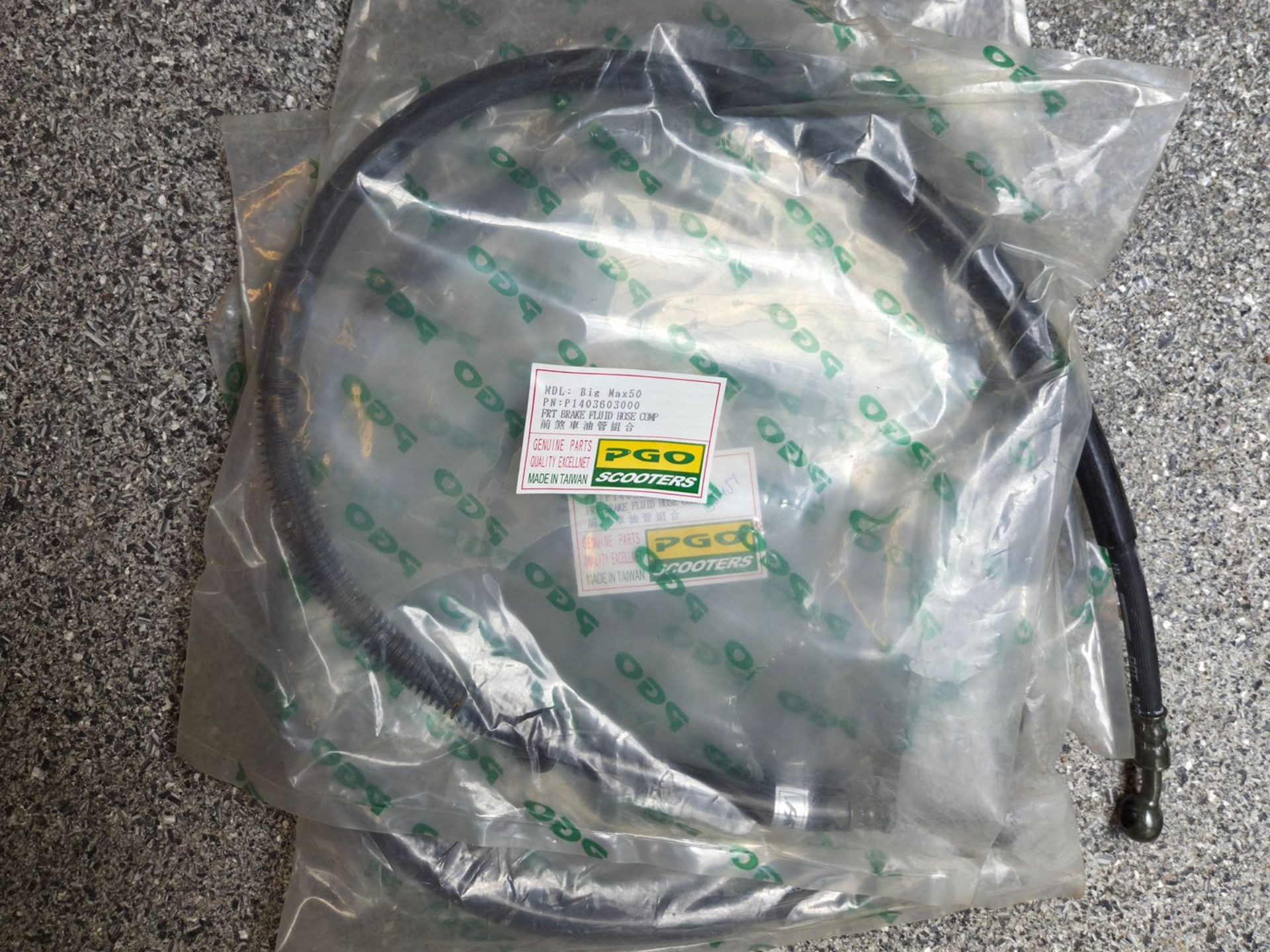 Een opgerolde zwarte kabel in een doorzichtige plastic verpakking op een grijs tapijt, met een klein etiketje eraan.