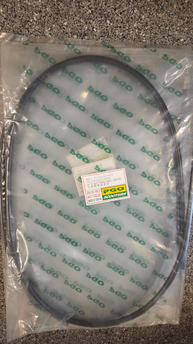 Een opgerolde zwarte kabel, verpakt in een doorzichtige plastic zak met een klein etiketje, ligt op een ruw vloeroppervlak.