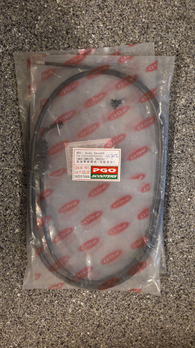 Een doorzichtige plastic zak met een opgerolde zwarte kabel en een klein rood-wit label op een grijs tapijt.