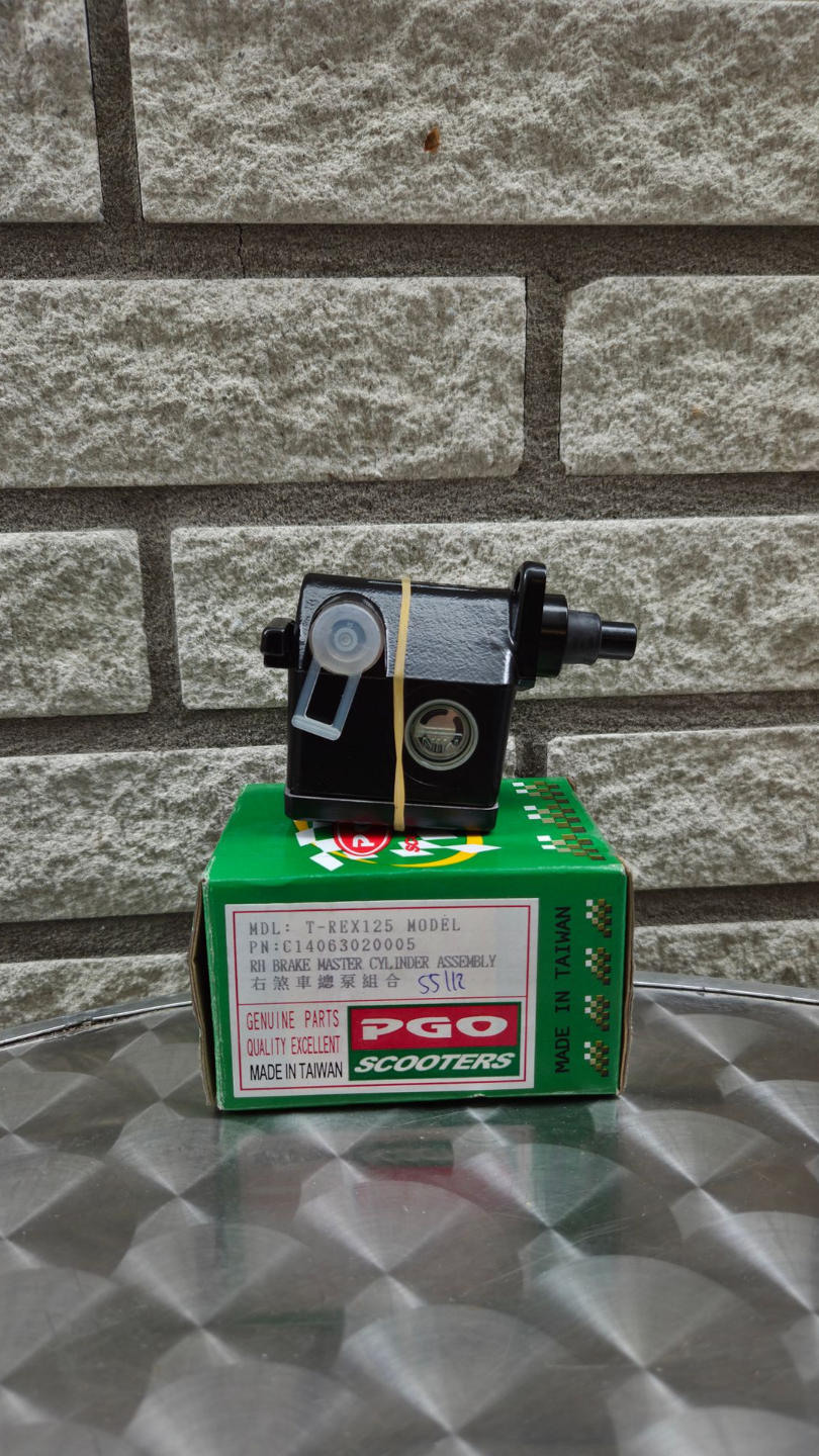 Een klein zwart-zilveren motortje op een groene doos, die op een metalen ondergrond tegen een bakstenen muur staat.