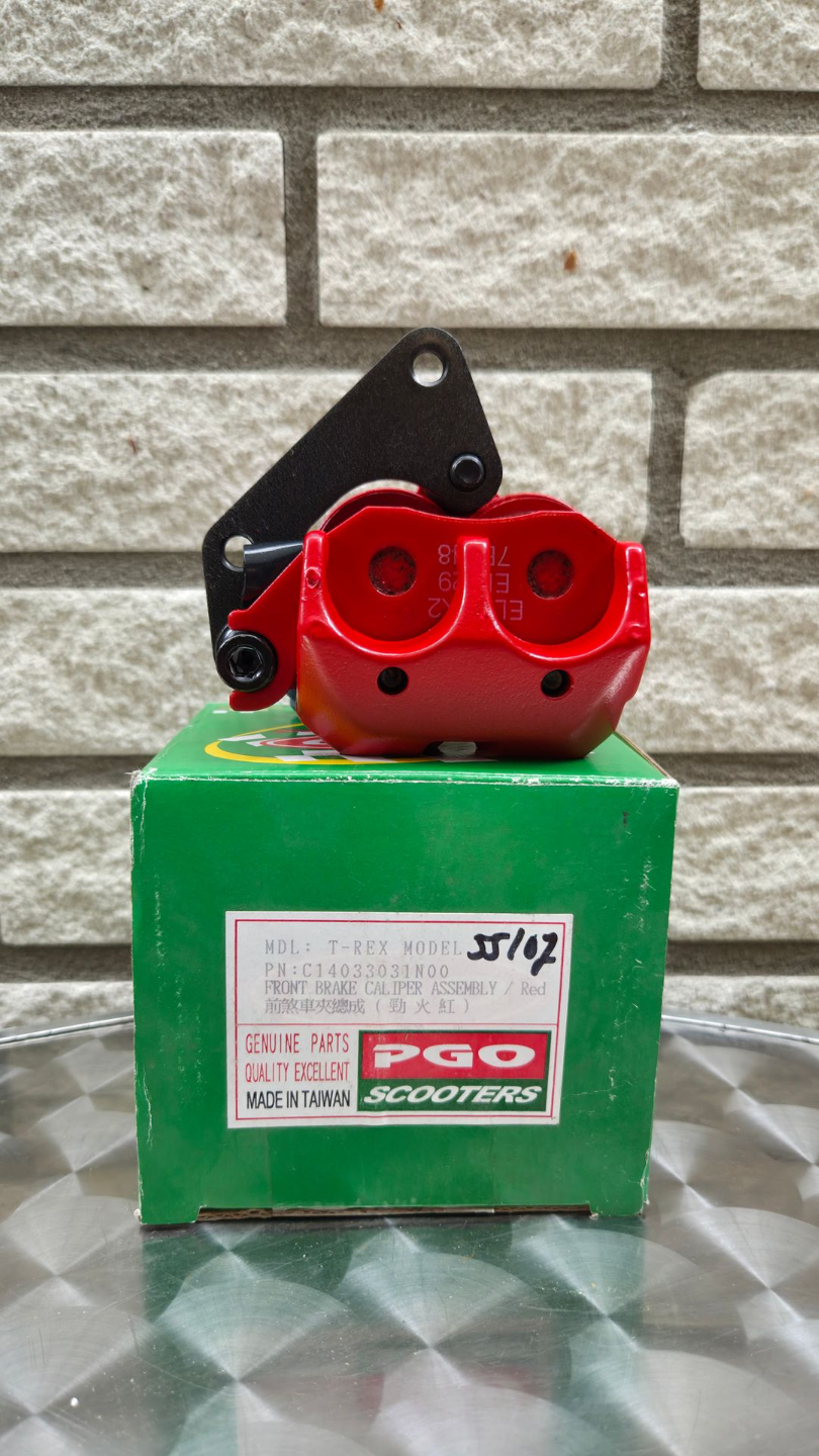 Rood apparaat met zwart handvat, gemonteerd op een groene doos tegen een bakstenen muur.
