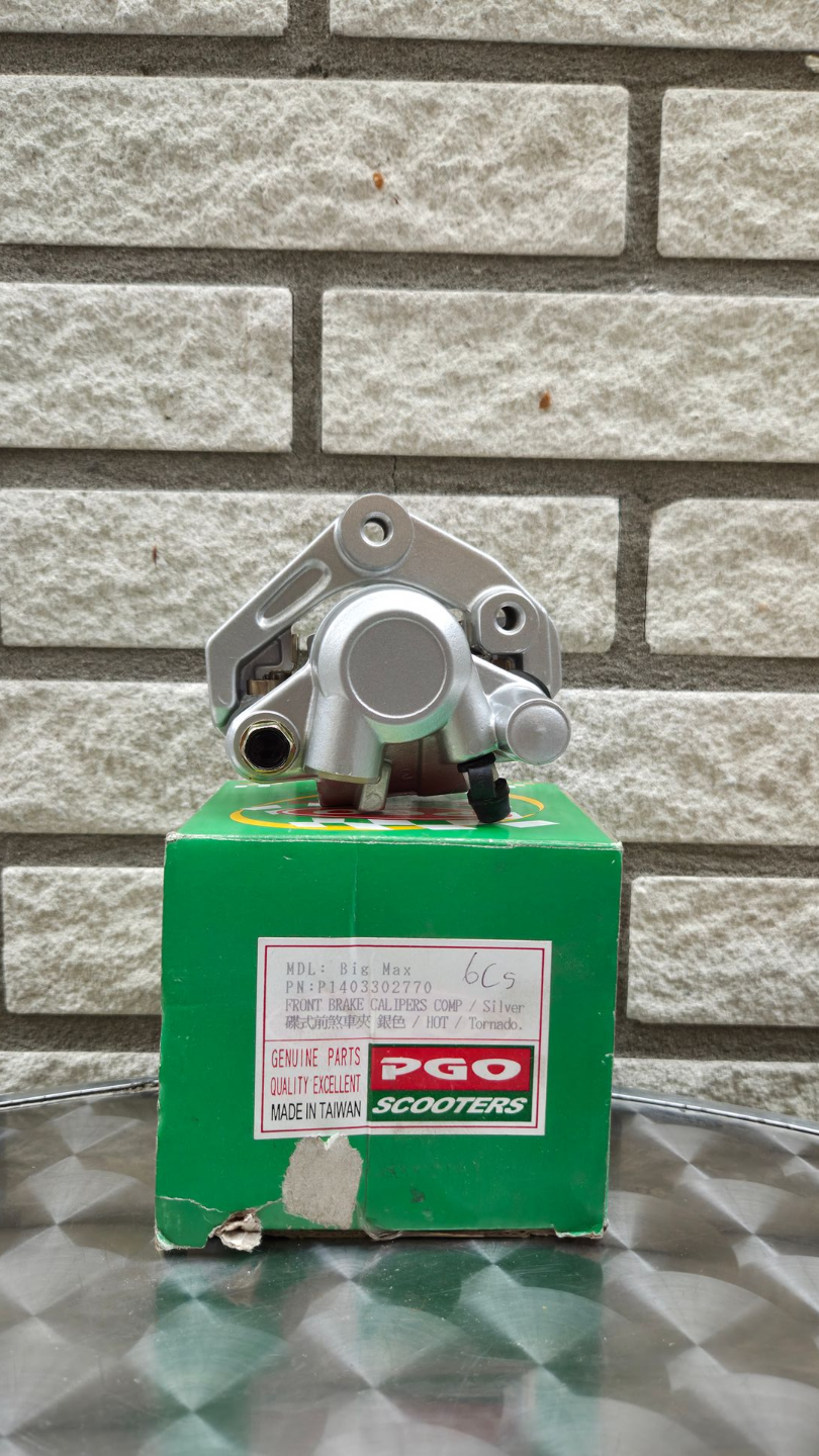 Groen machineonderdeel met metalen onderdelen aan de bovenkant, tegen een achtergrond van een bakstenen muur.