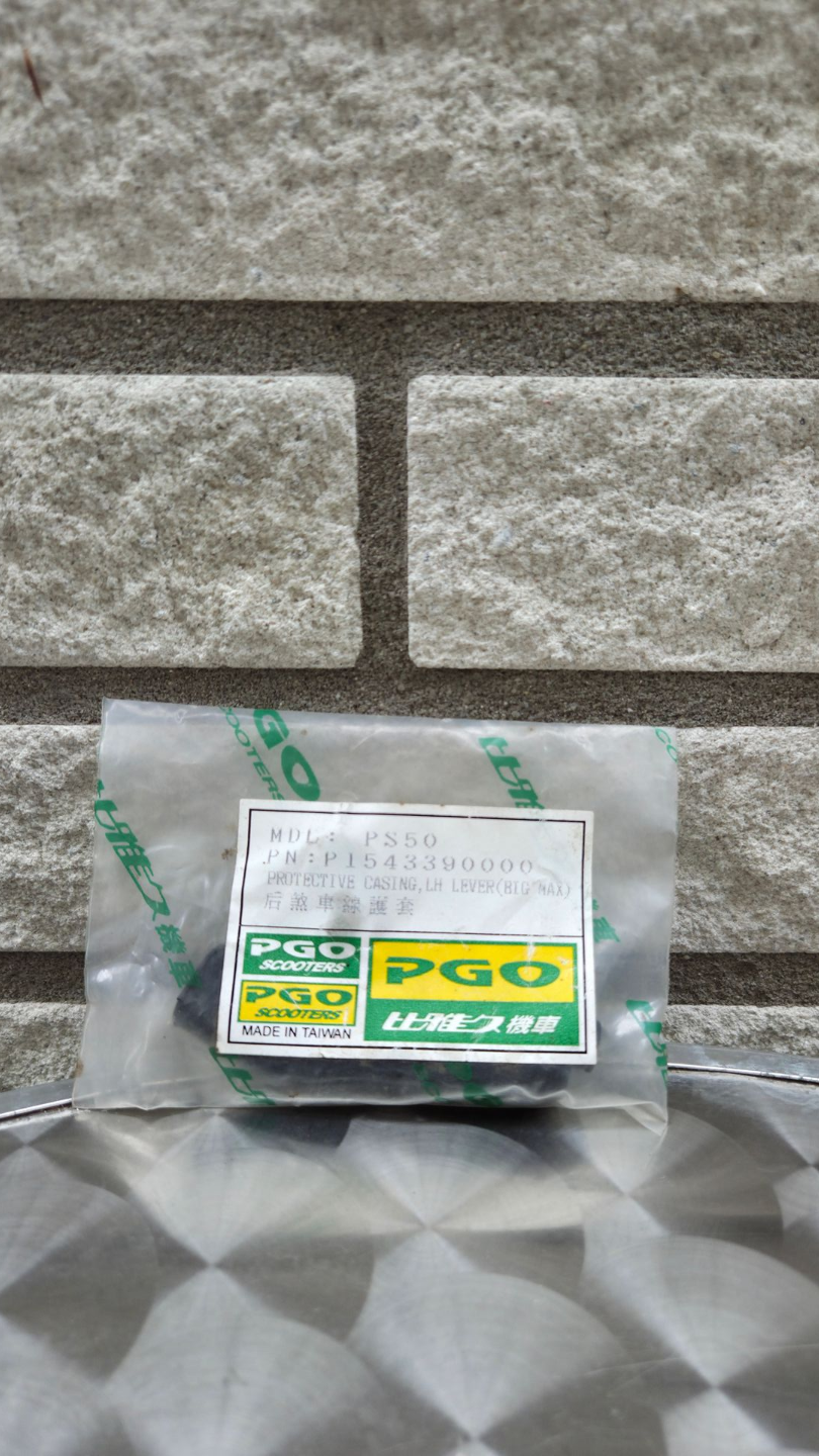 Een klein groen-wit PGO-doosje staat op een zilverkleurig oppervlak tegen een grijze bakstenen muur.