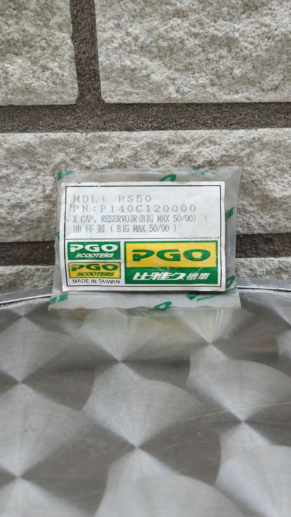 Kleine groen-witte productdoos met Japanse tekst op een zilverkleurig, gewatteerd oppervlak tegen een stenen muur.