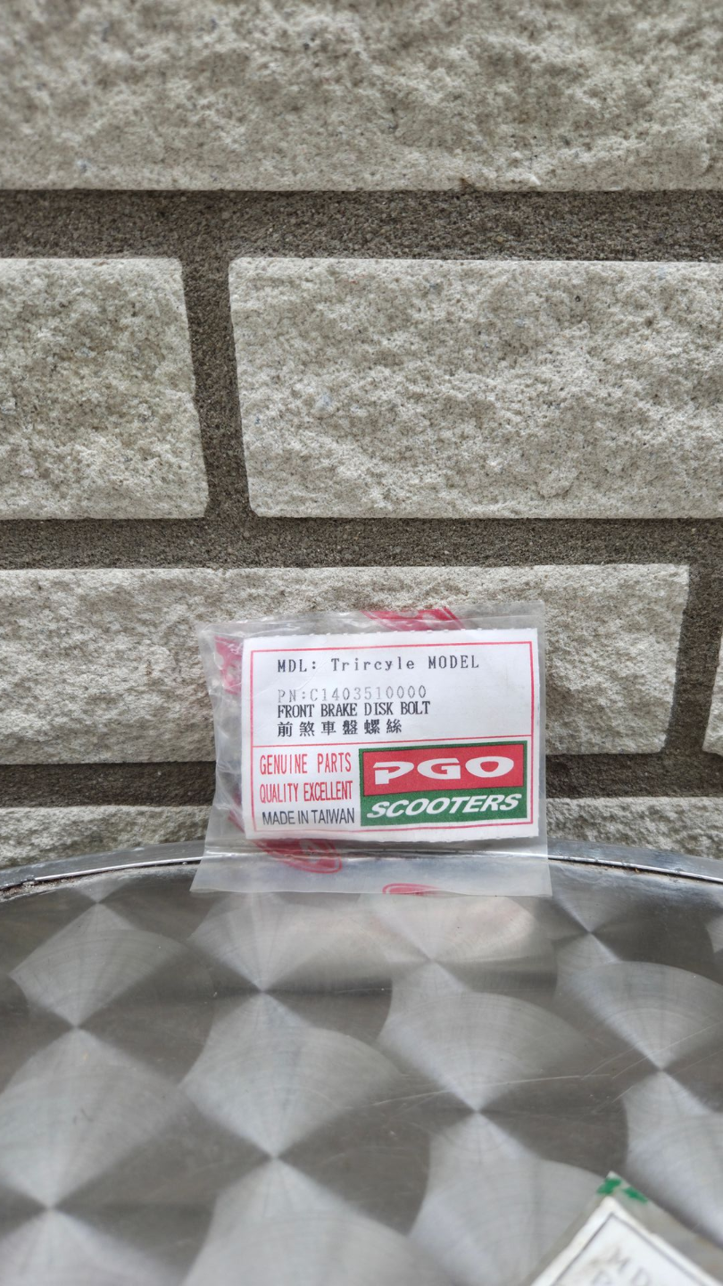 Klein productdoosje met rood-wit etiket op een metalen ondergrond met patroon, tegen een stenen muur.