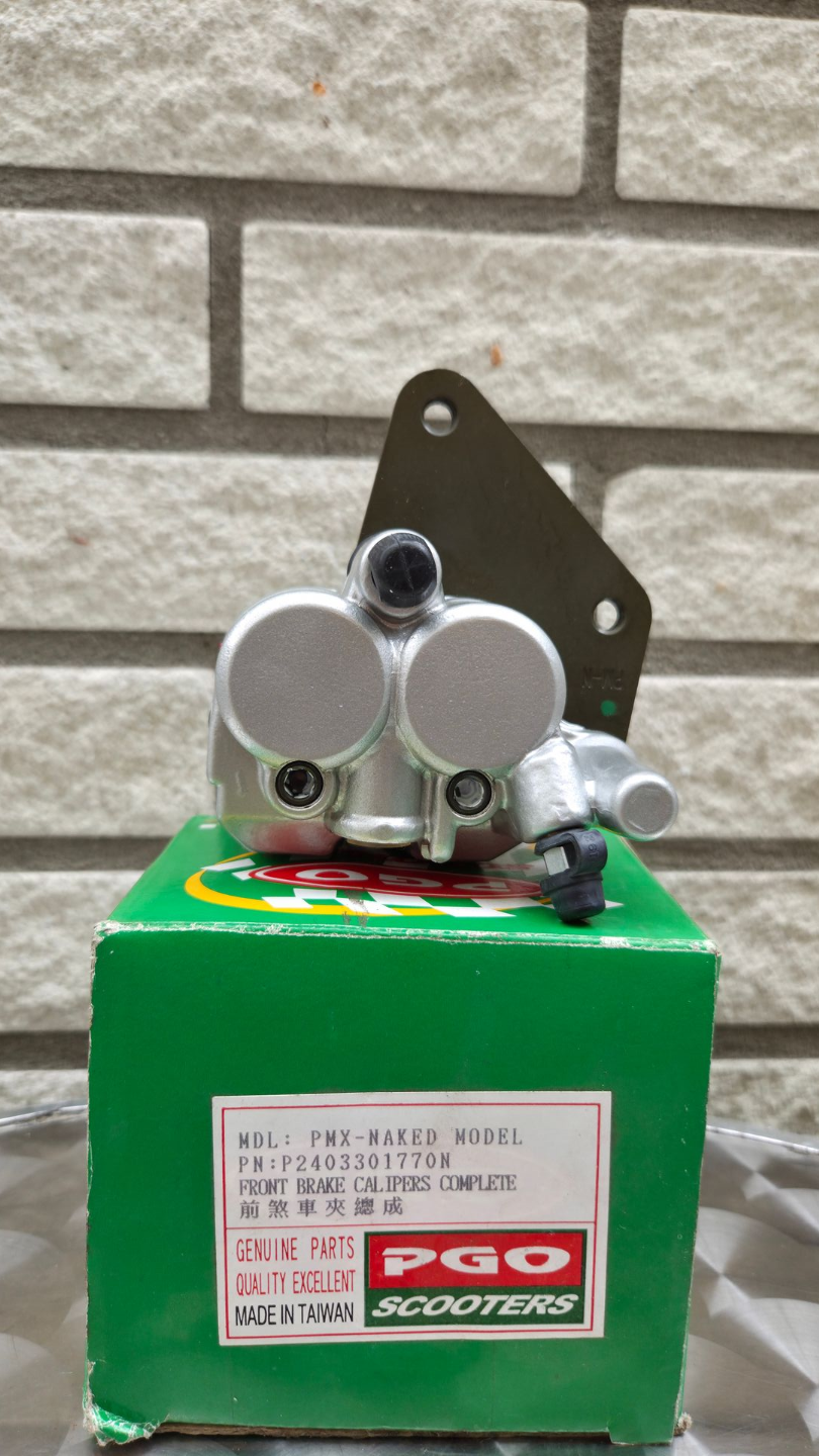 Klein groen apparaatje met zilverkleurige onderdelen en een rood label, gefotografeerd tegen een grijze bakstenen muur.