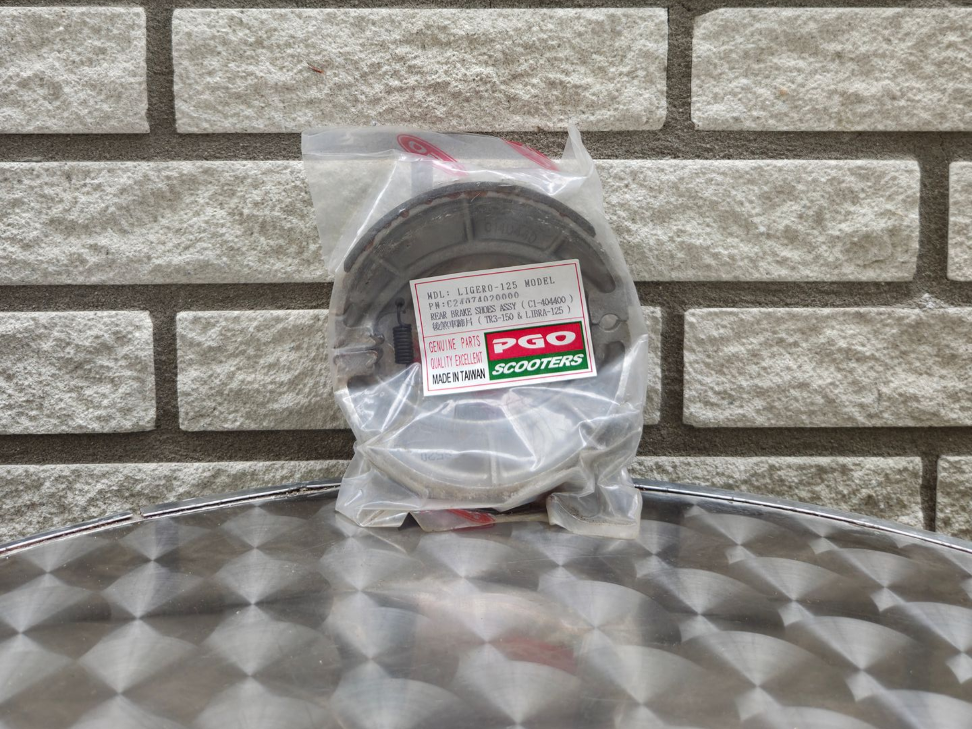 Een doorzichtige plastic zak met een zwarte kabel of snoer ligt op een zilverkleurige, gestructureerde ondergrond tegen een bakstenen muur.