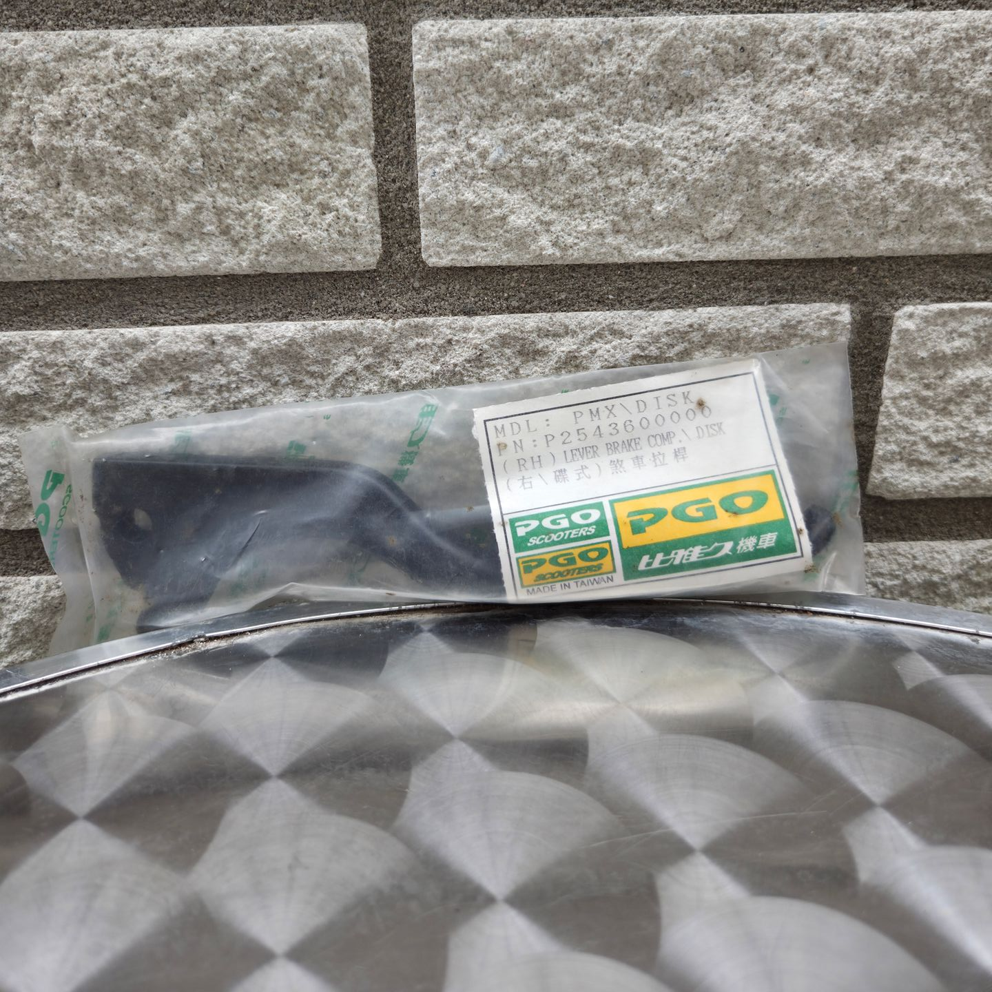 Plastic tas met een zwart voorwerp en een groen-wit etiket op een stenen muurachtergrond.