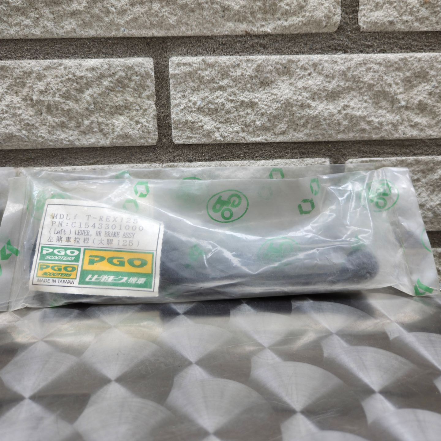 Een doorzichtige plastic zak met een donker, opgevouwen voorwerp erin, die op een gestructureerde grijze ondergrond tegen een stenen muur ligt.