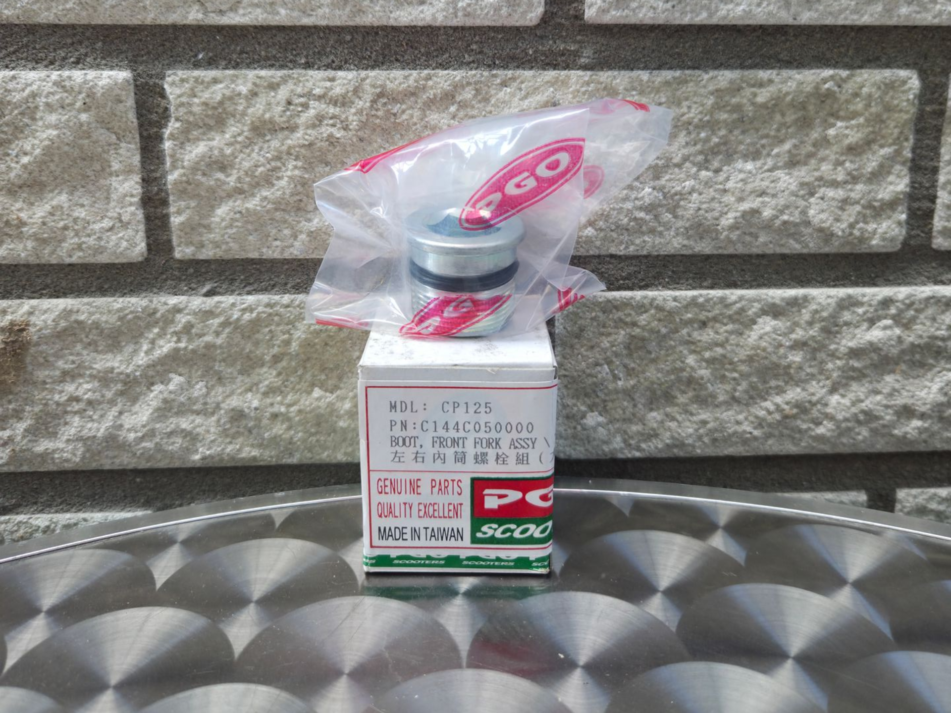 Klein doosje met een roze-wit etiket aan de bovenkant, verpakt in plastic, op een metalen ondergrond met structuur.