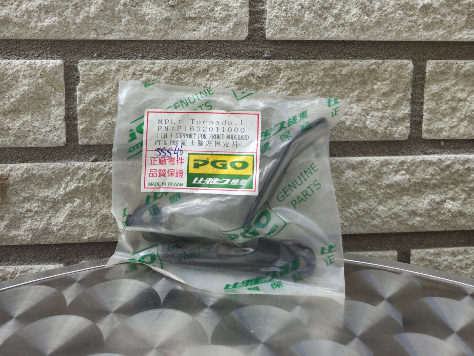 Een doorzichtige plastic verpakking met een groen etiket ligt op een grijs, patroonrijk oppervlak tegen een bakstenen muur.