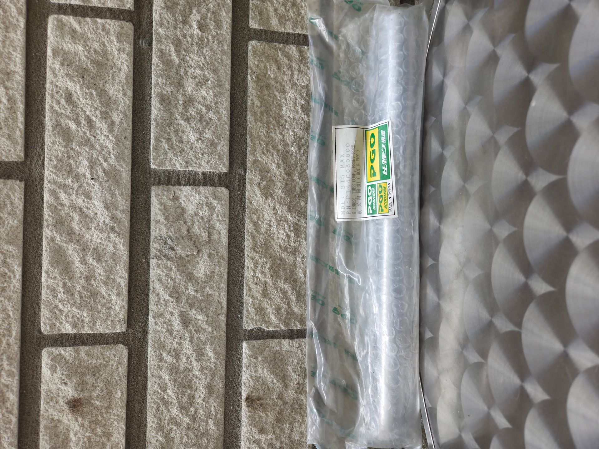 Een cilindrisch voorwerp, verpakt in transparant plastic, met een groen-wit etiket op een grijs, gestructureerd oppervlak.