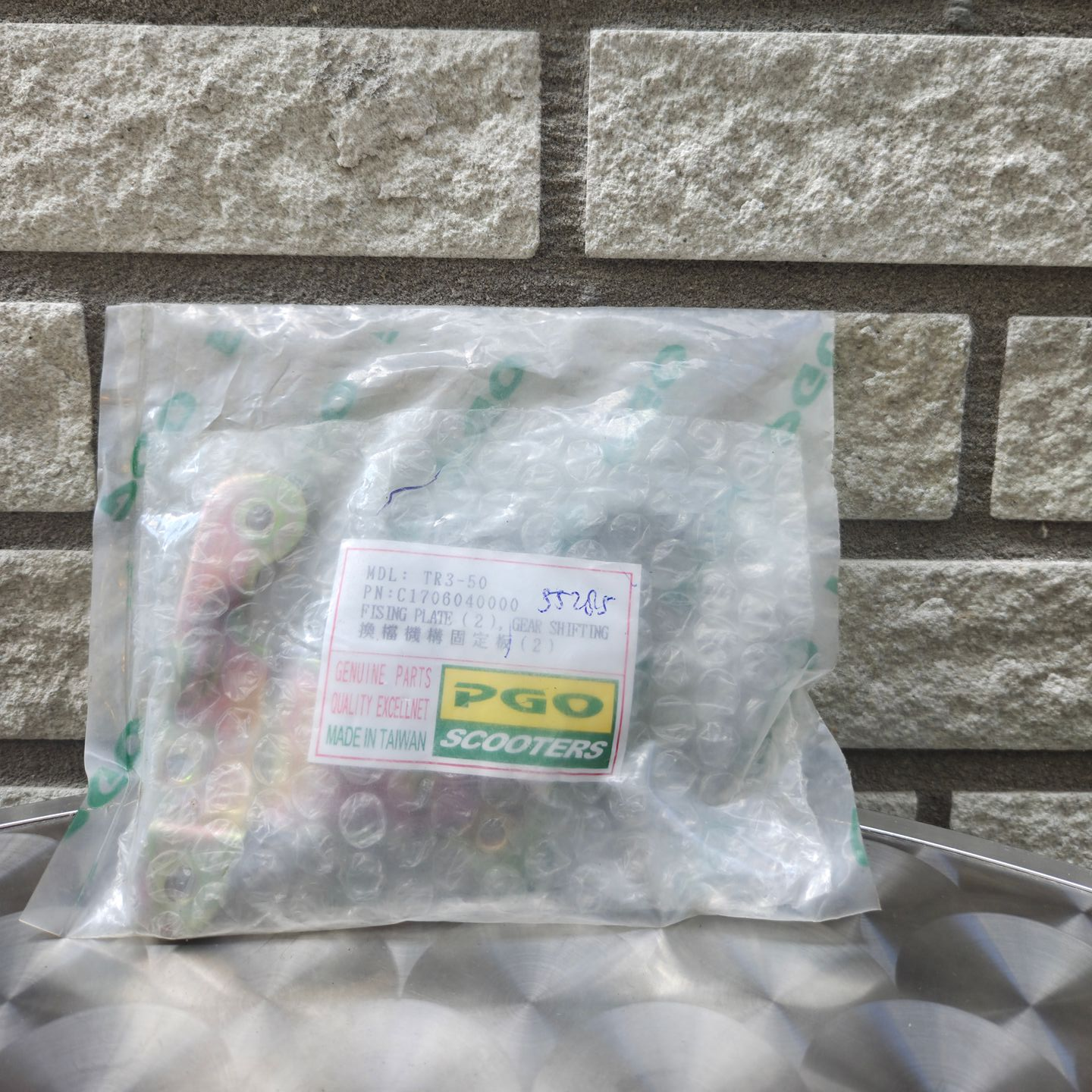 Een doorzichtige plastic zak met een etiket erop ligt op een metalen ondergrond tegen een stenen muur.