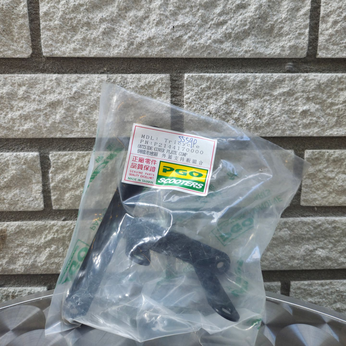 Een doorzichtige plastic zak met een zwarte metalen beugel hangt tegen een grijze bakstenen muur.