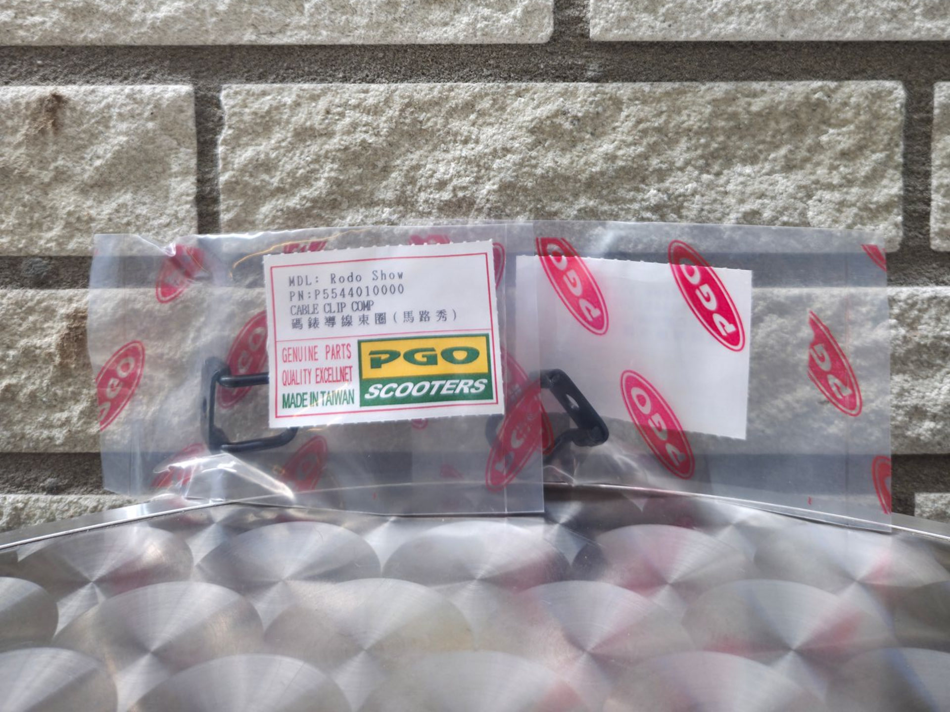 Een doorzichtige plastic zak met een etiket en kleine verpakte artikelen tegen een stenen muur.