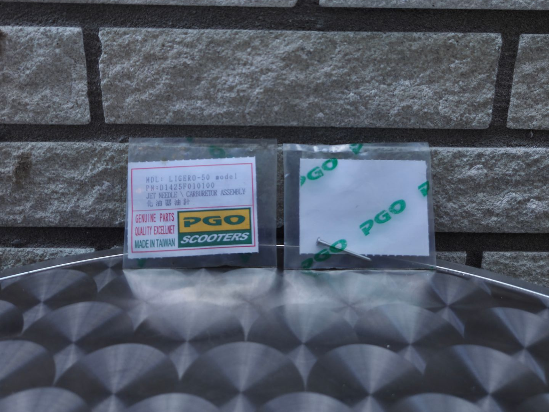 Twee kleine PGO-onderdelenpakketten op een oppervlak met patroon tegen een stenen muur.