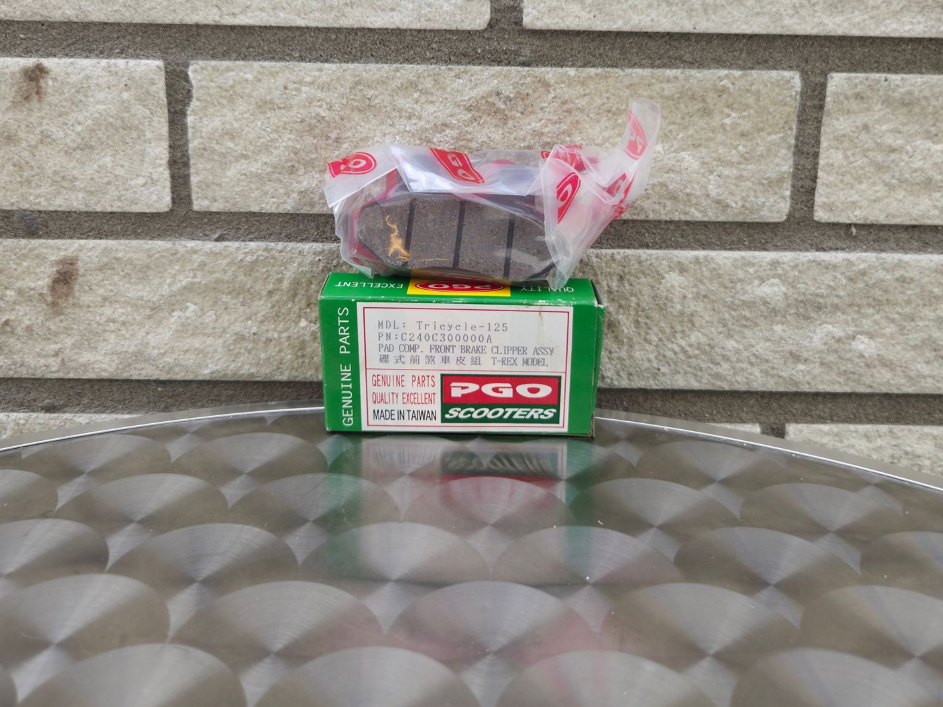 Ingepakt artikel in een groene P&G-doos op een metalen tafel, tegen een bakstenen muur.