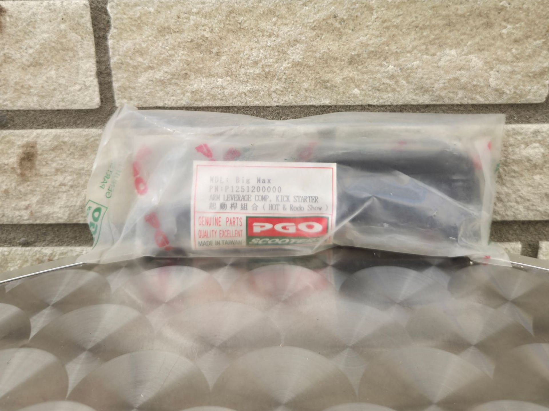 Een plastic zak met een rood-wit etiket op een tafelblad met een patroon, tegen een stenen muur.