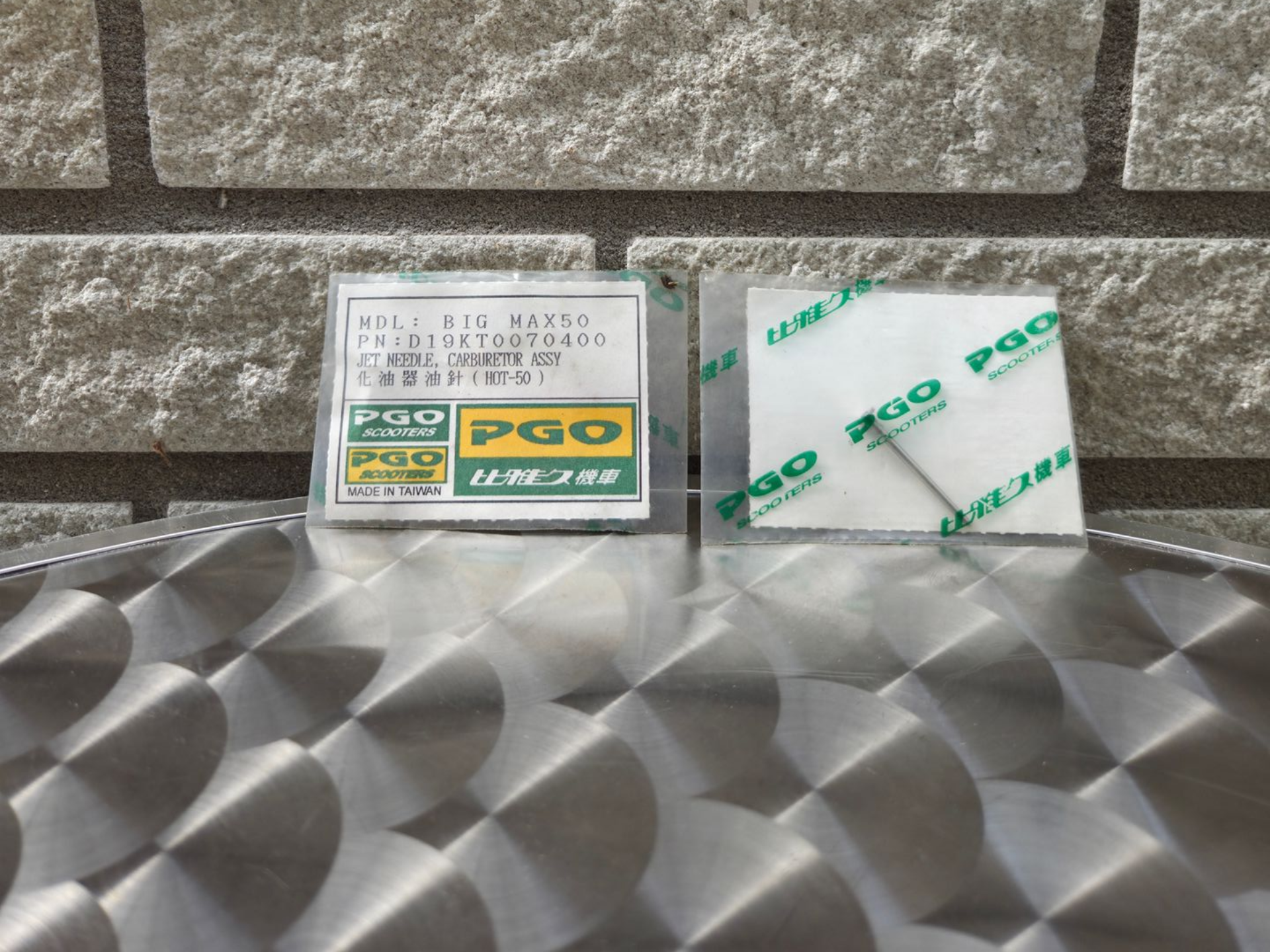 Twee kleine doosjes op een metalen ondergrond tegen een stenen muur, waarvan er één is gemerkt met PQQ.