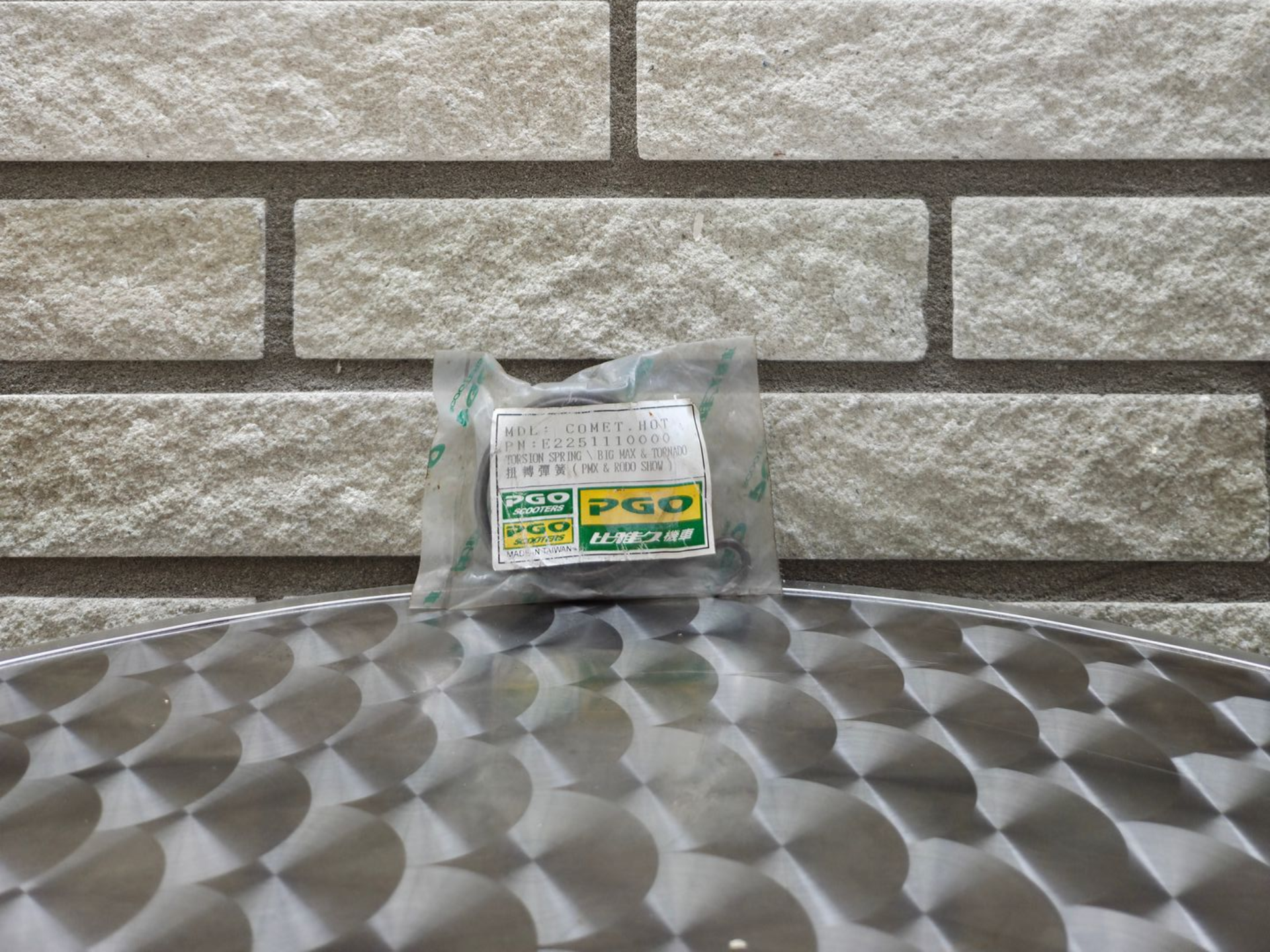 Klein, doorzichtig pakketje met groen etiket op een tafelblad met patroon tegen een bakstenen muur.