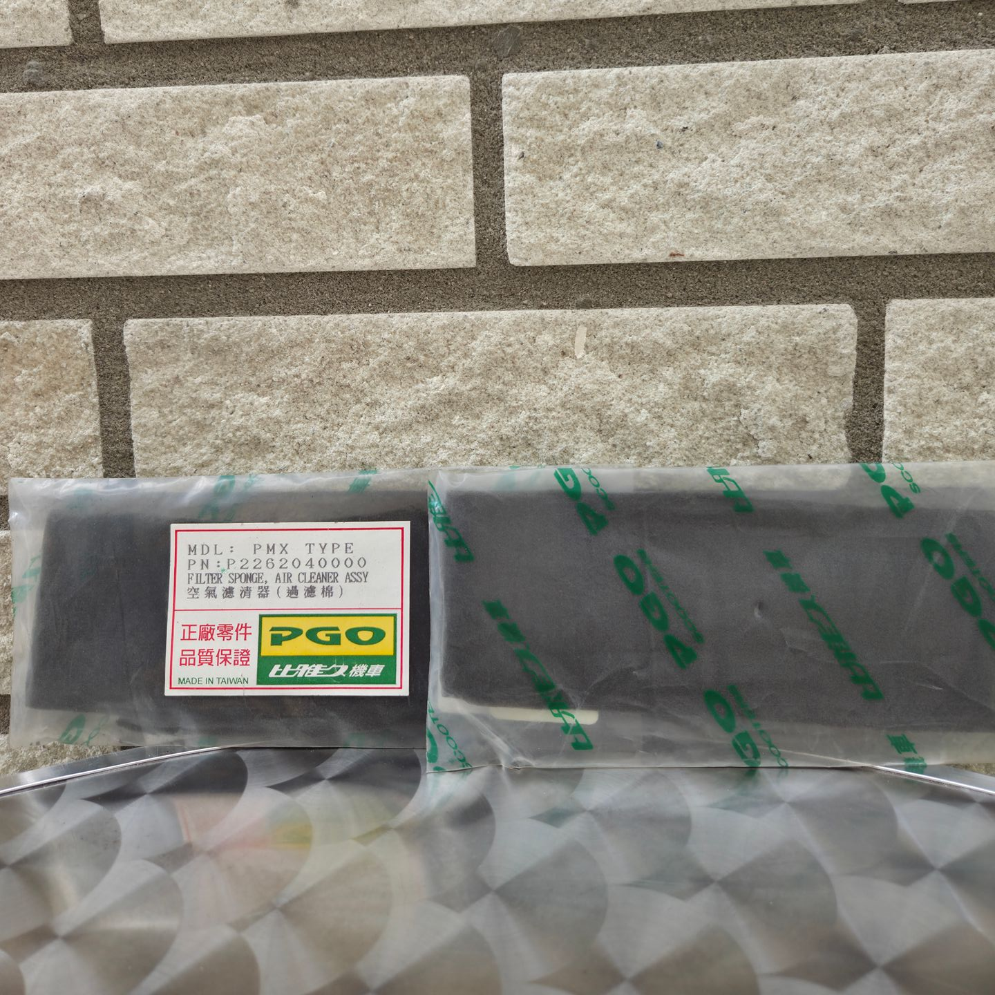 Een in plastic verpakt pakket met een PGO-etiket, rustend op bubbeltjesplastic tegen een stenen muur.