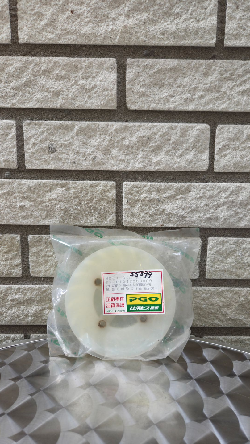 In plastic verpakt rond kaaswiel met etiket op een ondergrond met patroon, voor een bakstenen muur.