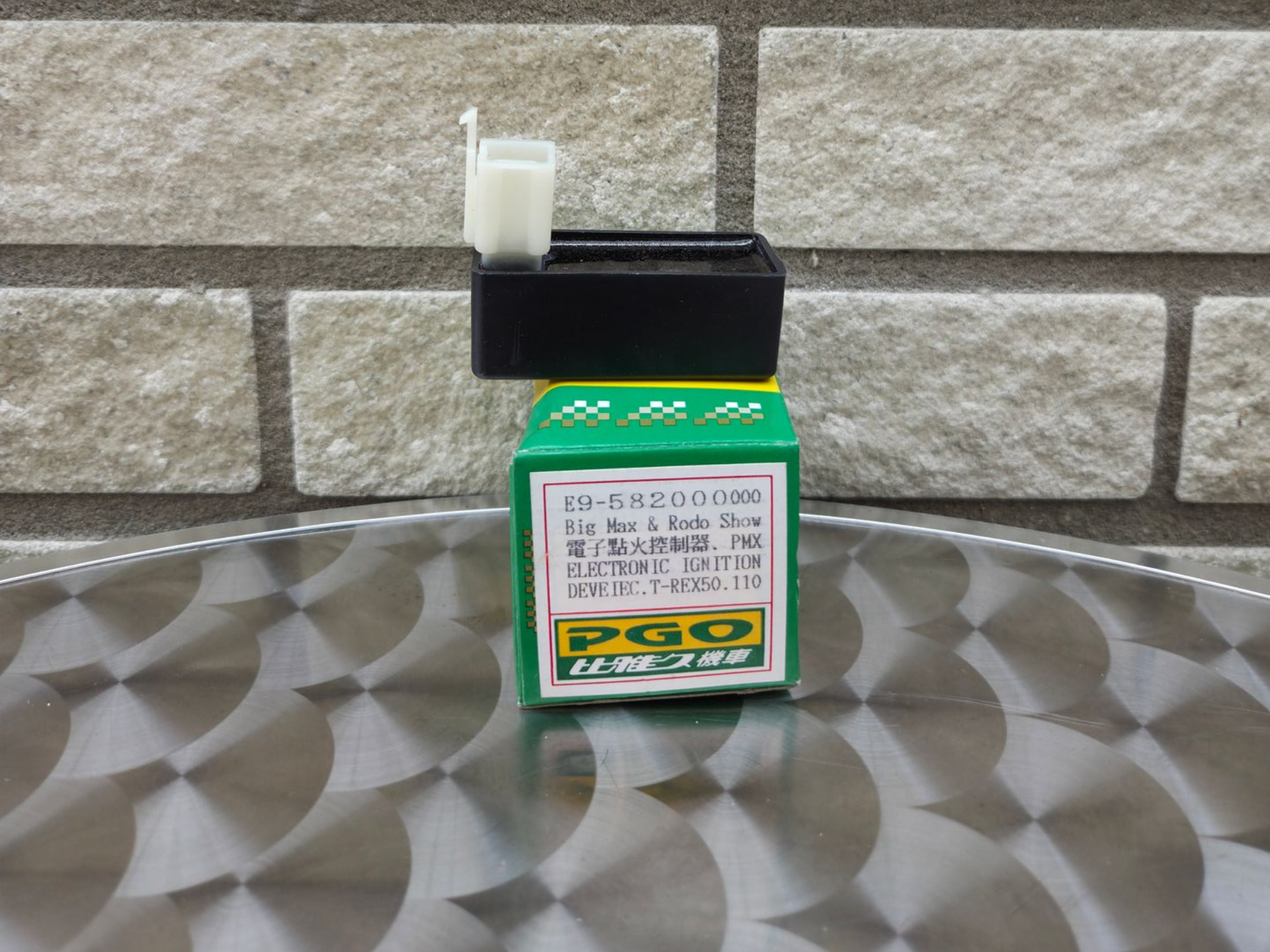Een plastic container met groen etiket, zwarte dop en witte tuit, staat op een tafel met patroon tegen een stenen muur.