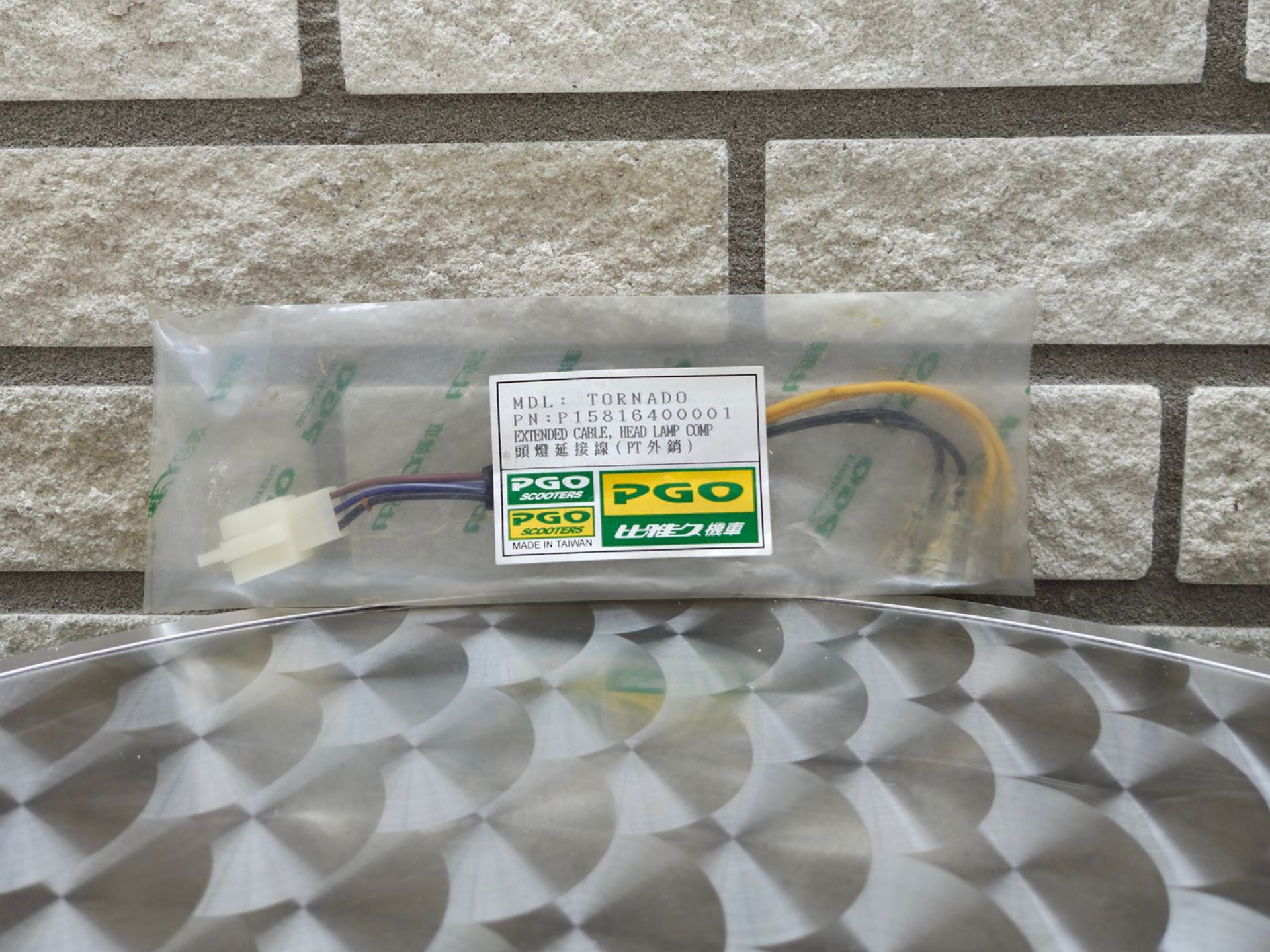 Een plastic zak met een klein, gelabeld kabeltje ligt op een grijs, patroonrijk oppervlak tegen een bakstenen muur.