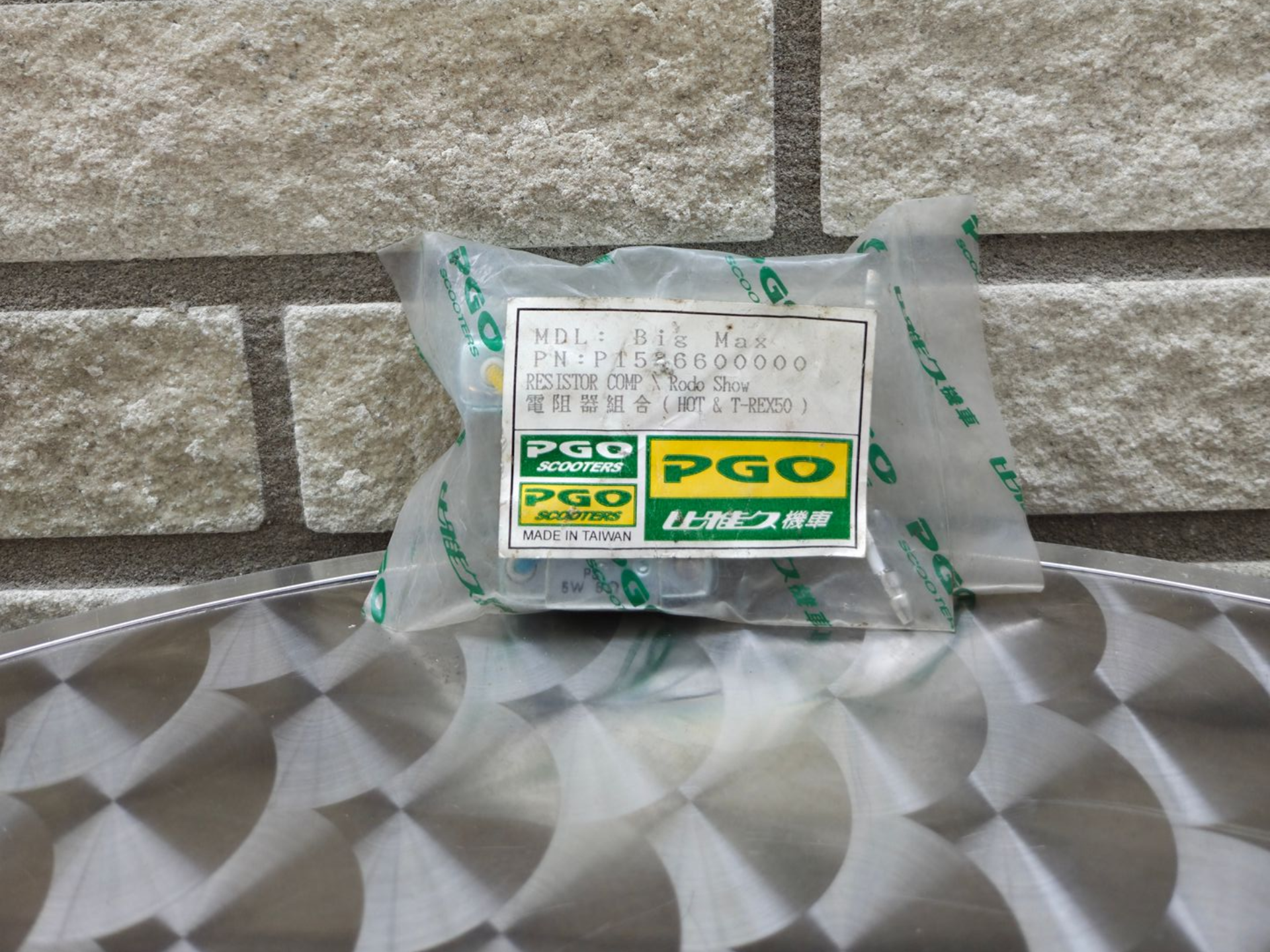 Een verpakte groen-gele doos PGS-tissue op een ondergrond met patroon tegen een stenen muur.