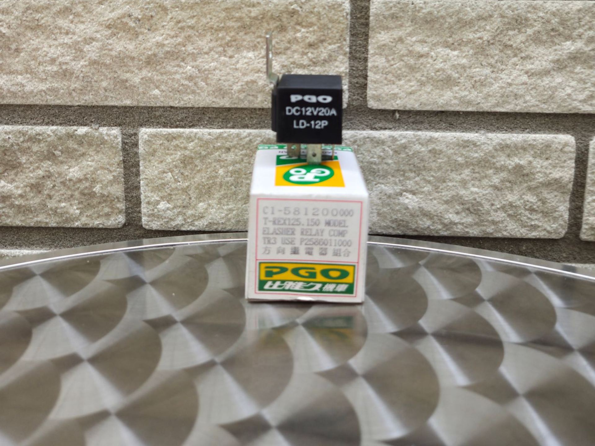 Zwarte DGO-doos op een wit-groene verpakking tegen een stenen muur op een ondergrond met een patroon.