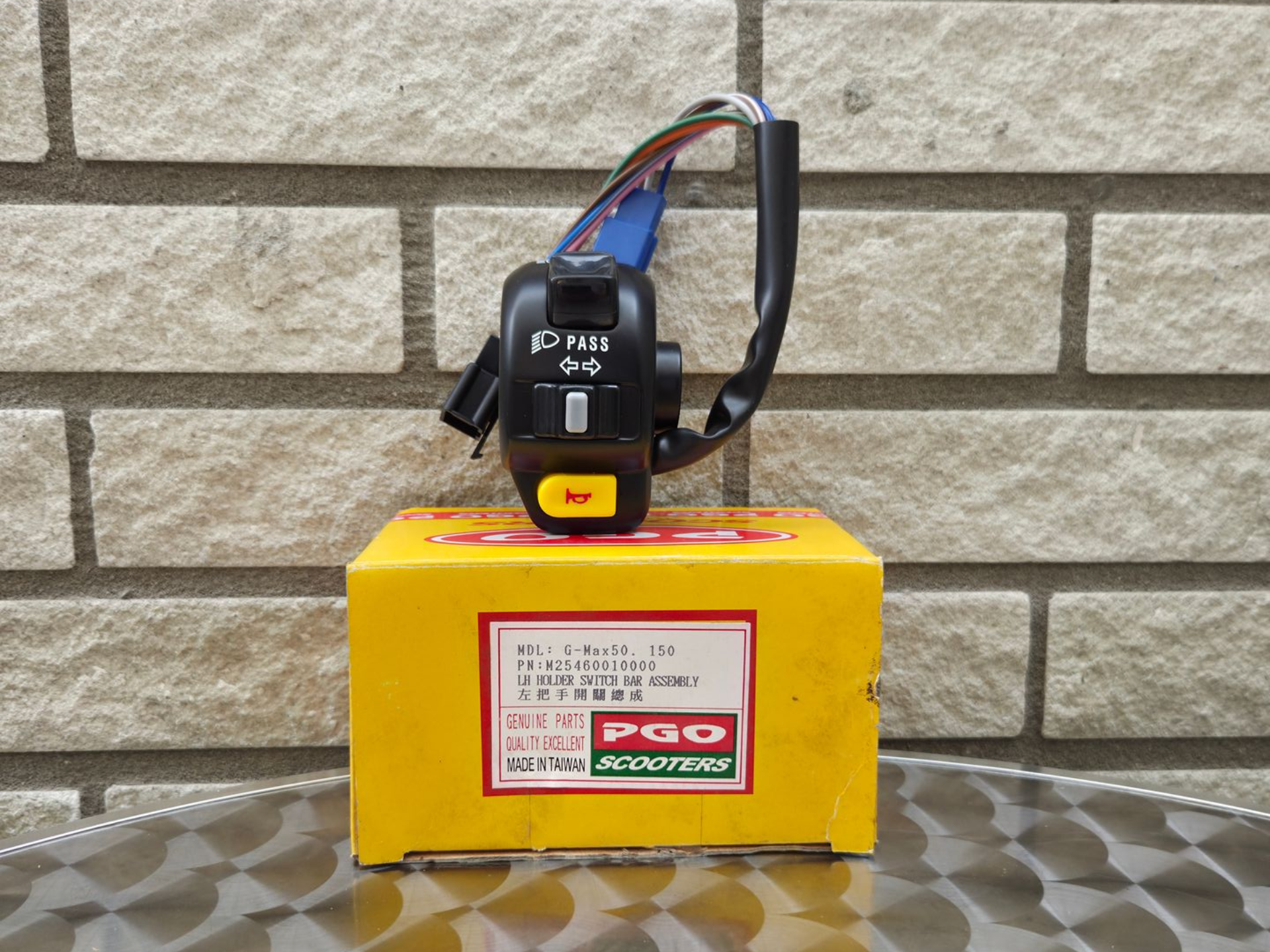 Gele doos met een zwart elektronisch apparaat erop, tegen een stenen muur.