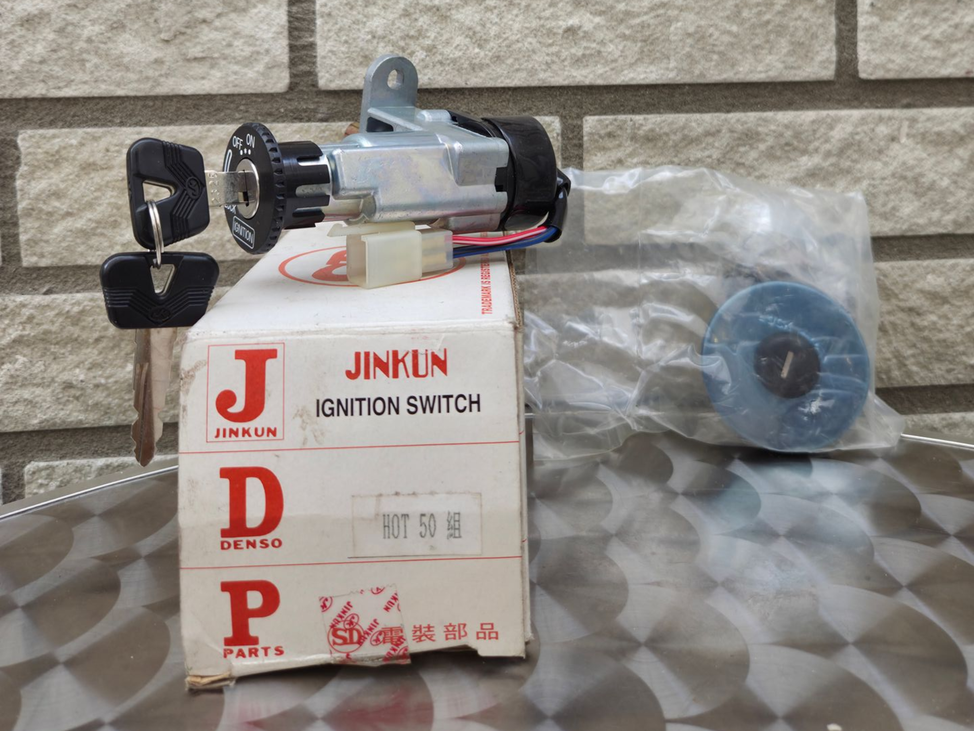 Jinkun contactslotset in doos met sleutels, zwarte en zilveren onderdelen en een blauw rond stuk in plastic verpakking.