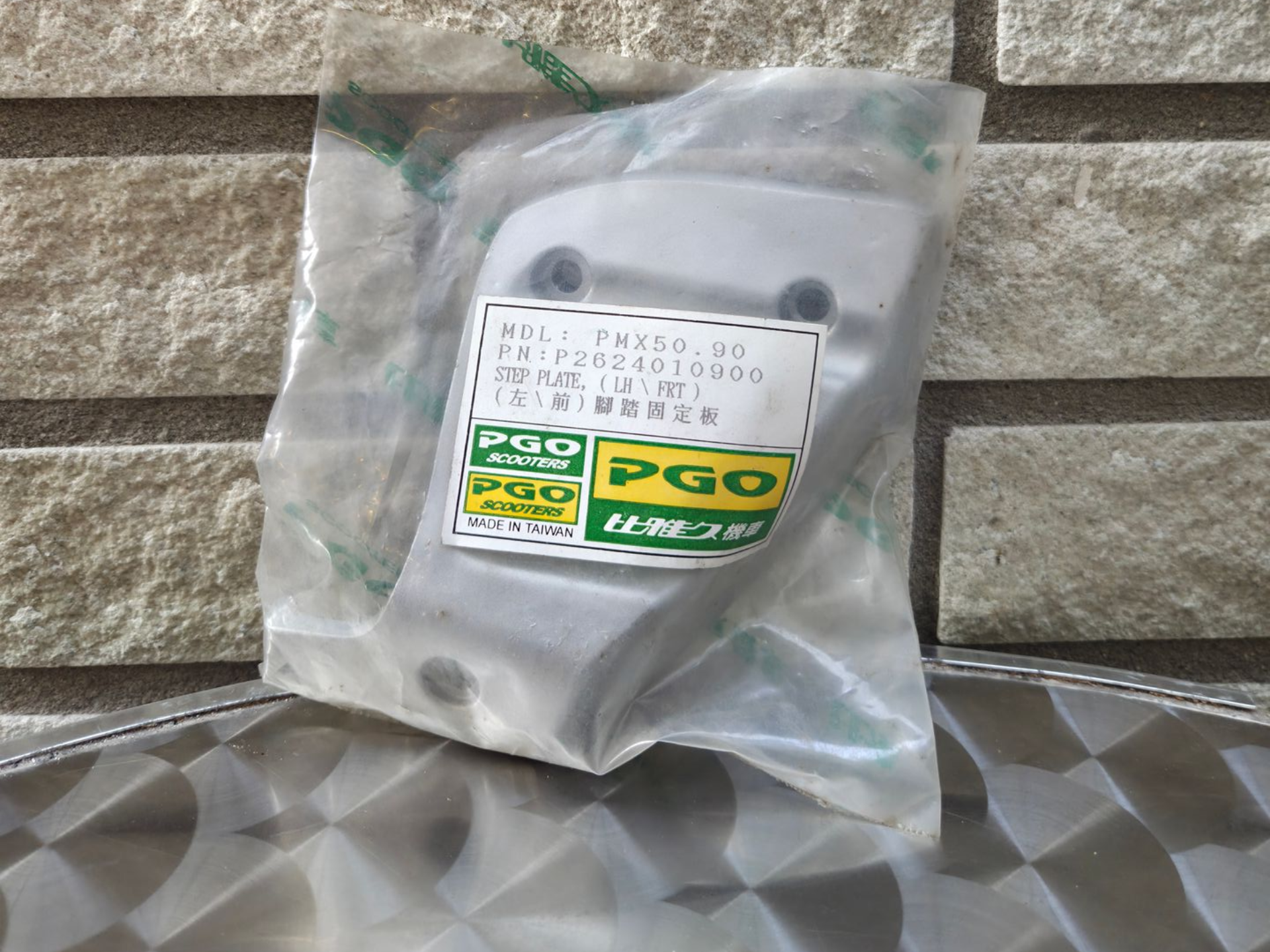Grijs metalen apparaat in een doorzichtige plastic zak met een geelgroen etiket, rustend op een gestructureerd oppervlak.