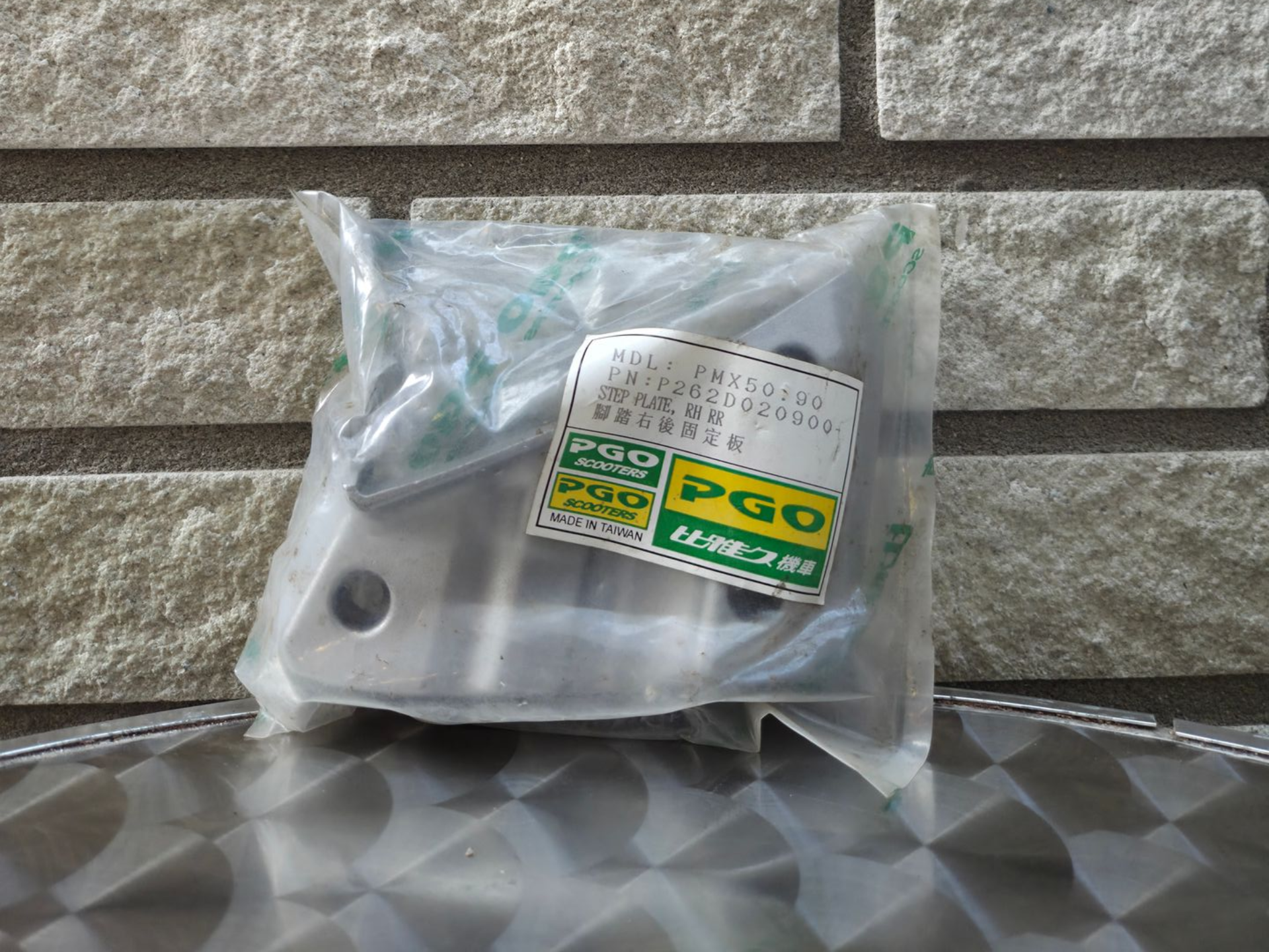 Doorzichtige plastic zak met een klein zilverkleurig metalen onderdeel en een groen-geel PGO-label op een tegeloppervlak.