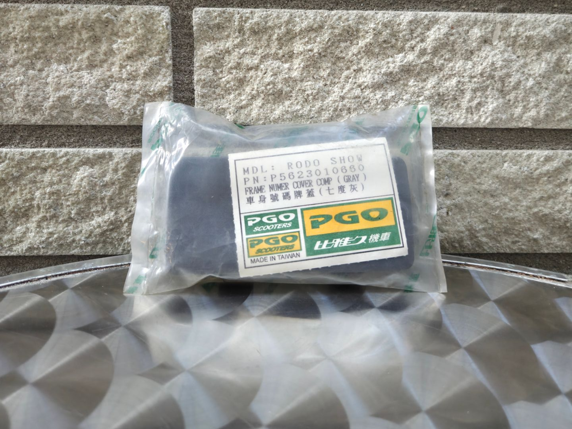 Een klein, doorzichtig plastic zakje met een donker rechthoekig voorwerp en een geelgroen etiket, tegen een stenen muur.
